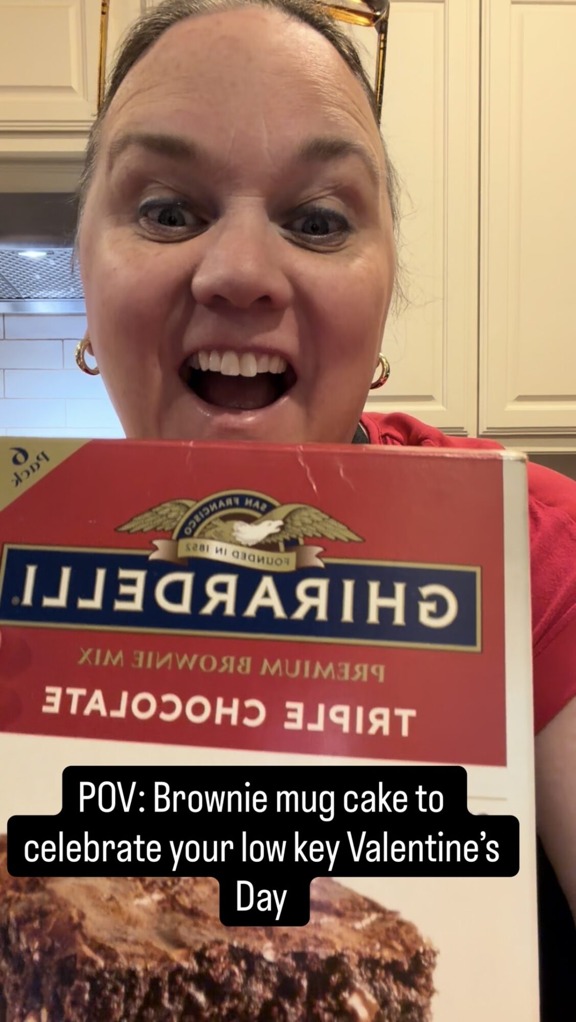 Person smiling with a brownie mug cake in front, kitchen background, celebrating Valentine's Day, with a red shirt.
