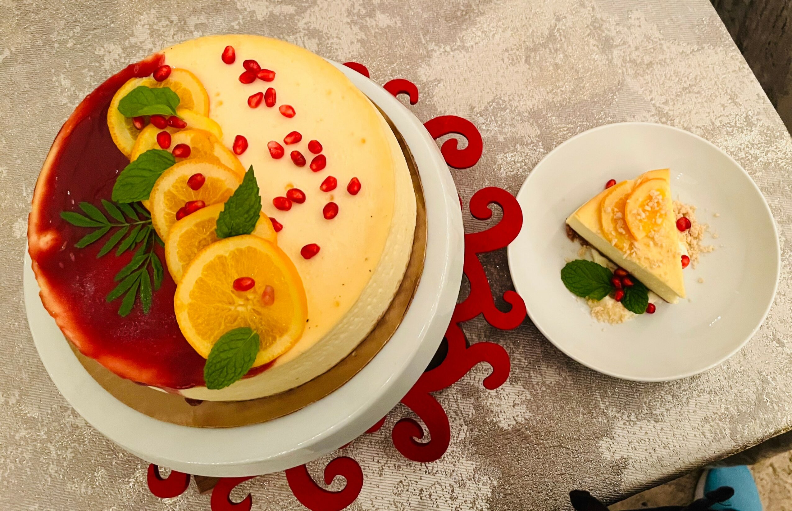 A decorated cheesecake with lemon slices, red berries, and green leaves on top, with a slice on a separate plate.