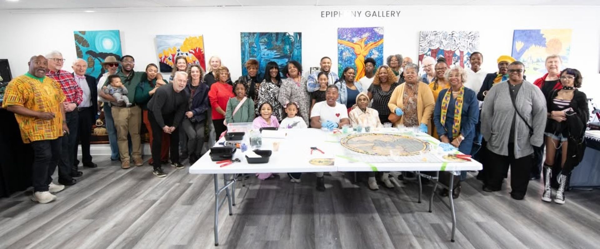 Group of people gathered around a table in an art gallery with colorful paintings on the wall.