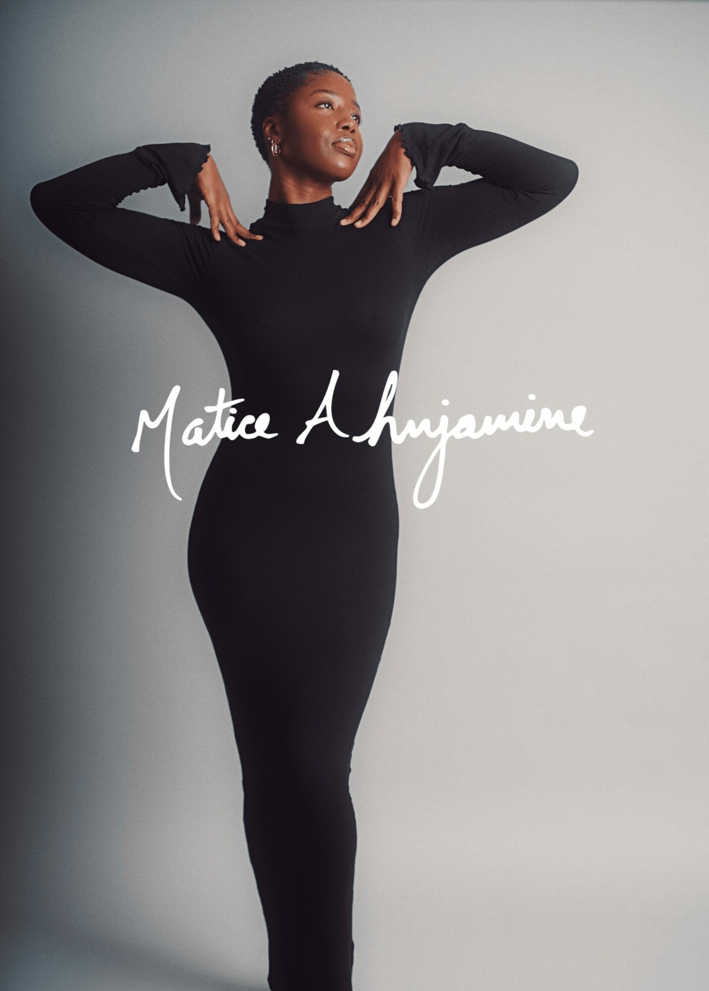 Woman in black dress with arms raised, smiling, against plain background, text overlay reads 'Matica A. Hyjamine'.