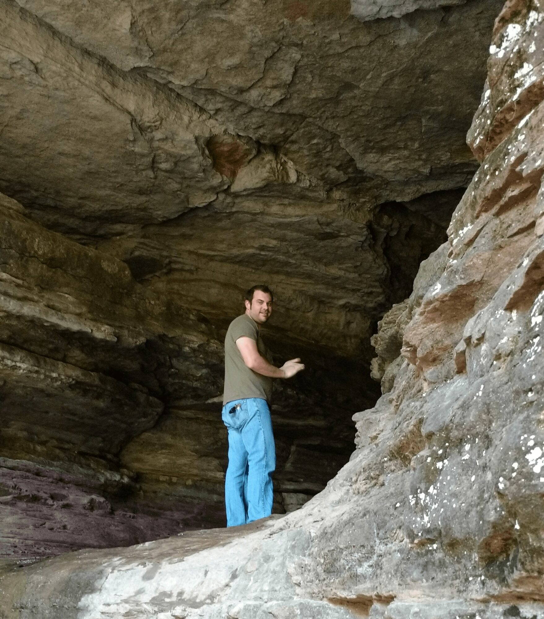 Person standing inside a large rocky cave, looking back over shoulder, surrounded by textured rock formations.