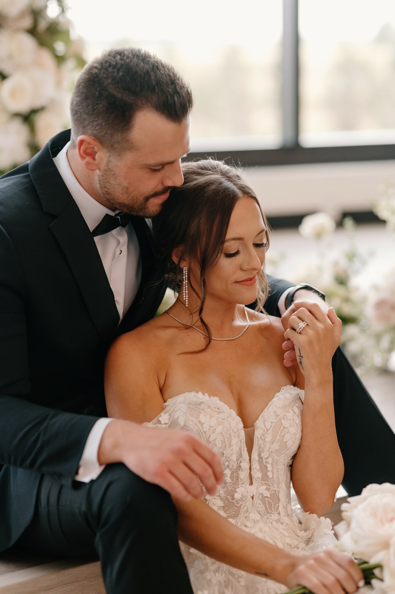 A man in a tuxedo and a woman in a wedding dress sit close together, with the man leaning over her shoulder.