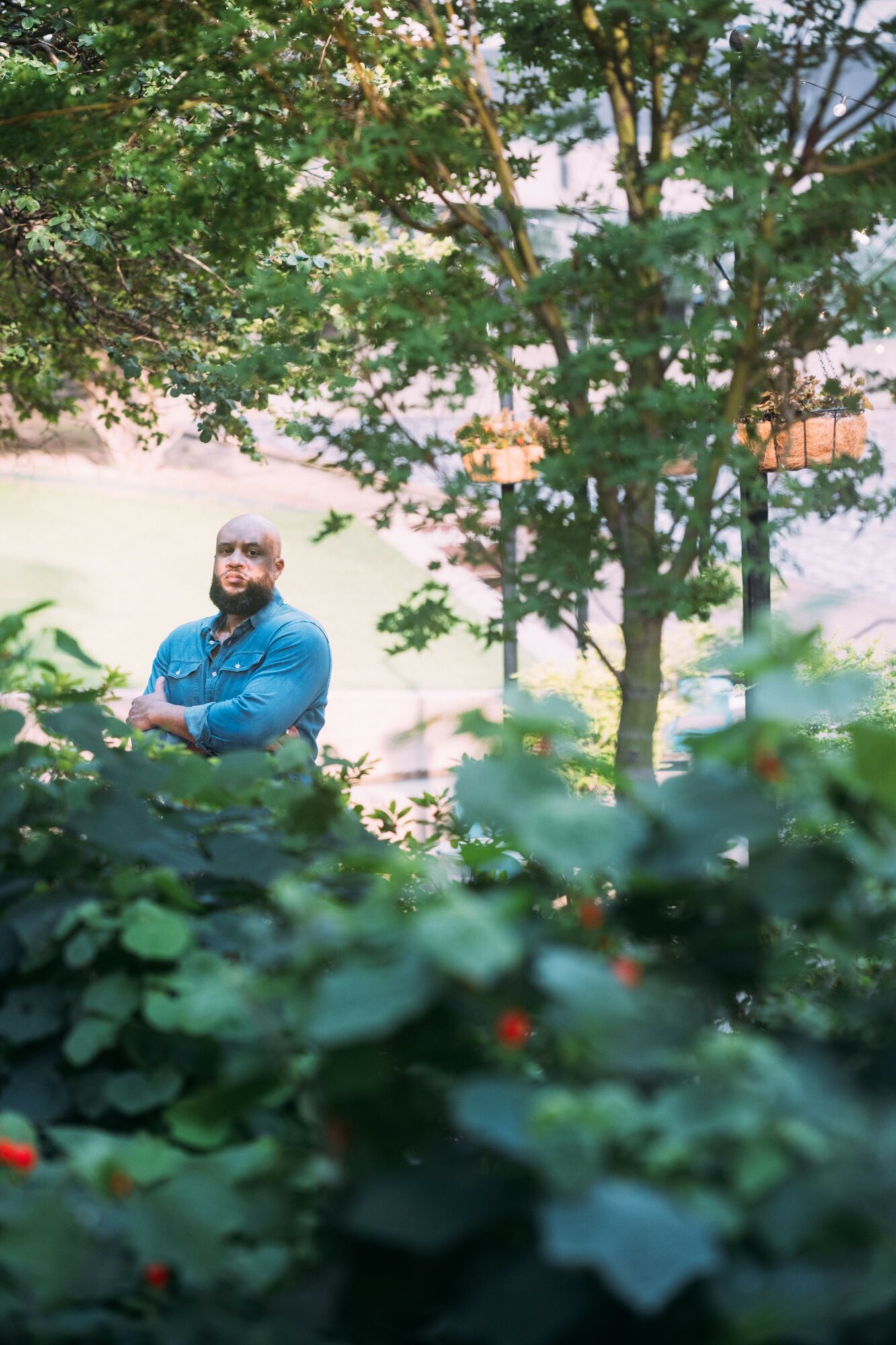 Man standing outdoors among trees and bushes, smiling, with sunlight filtering through leaves.