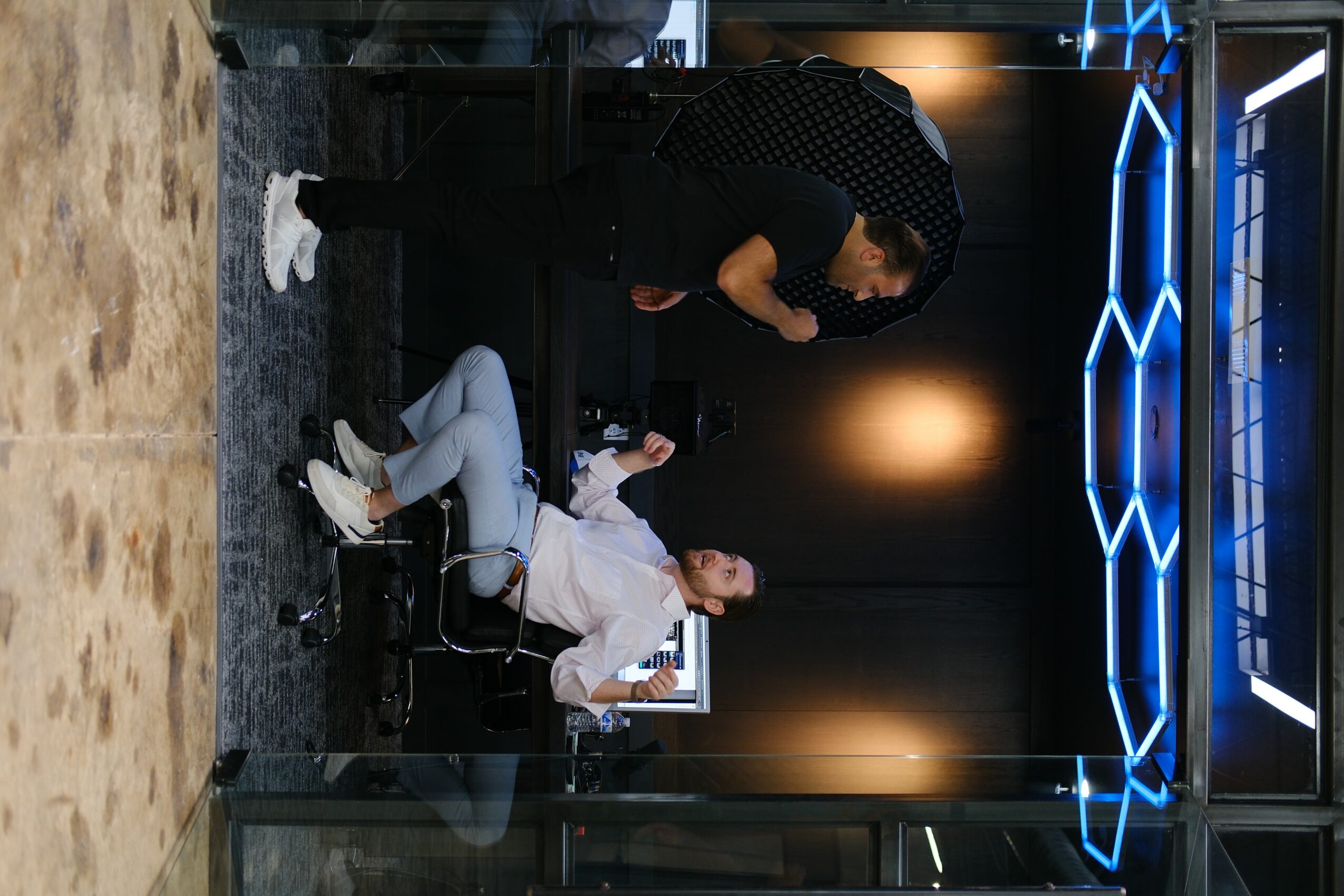 Person sitting at a desk talking to another person standing nearby in a modern room with blue neon lights.