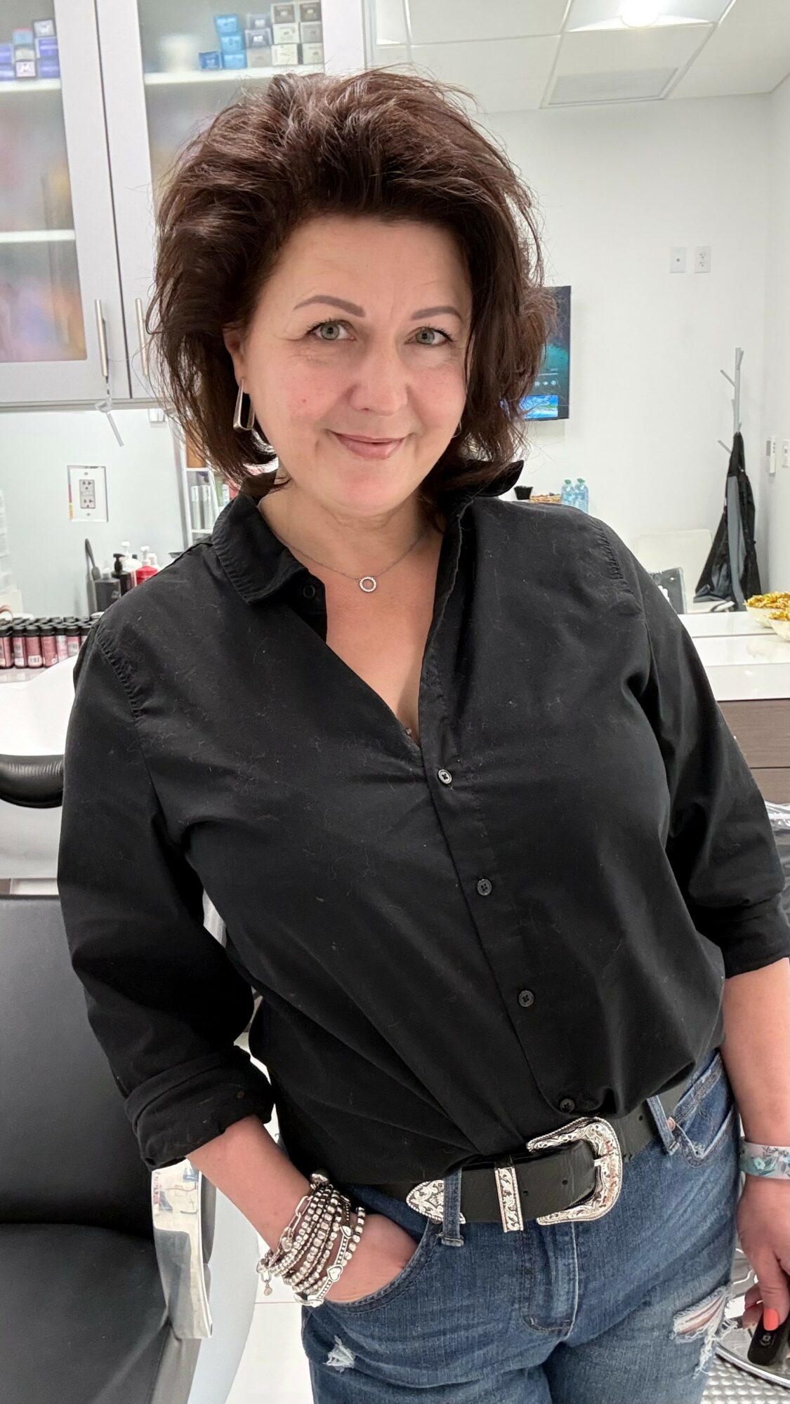 Woman with dark hair wearing a black shirt and jeans, standing in an office or lab environment.