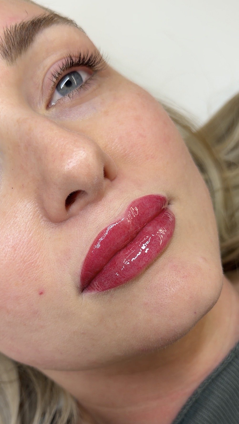 Close-up of a woman's face showing her eye, nose, and lips with glossy lipstick, light skin, and freckles.
