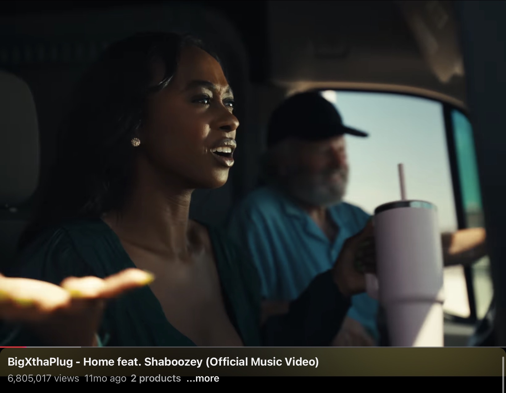 Two people sitting in a vehicle, with a woman in the foreground smiling and a man in the background holding a drink.