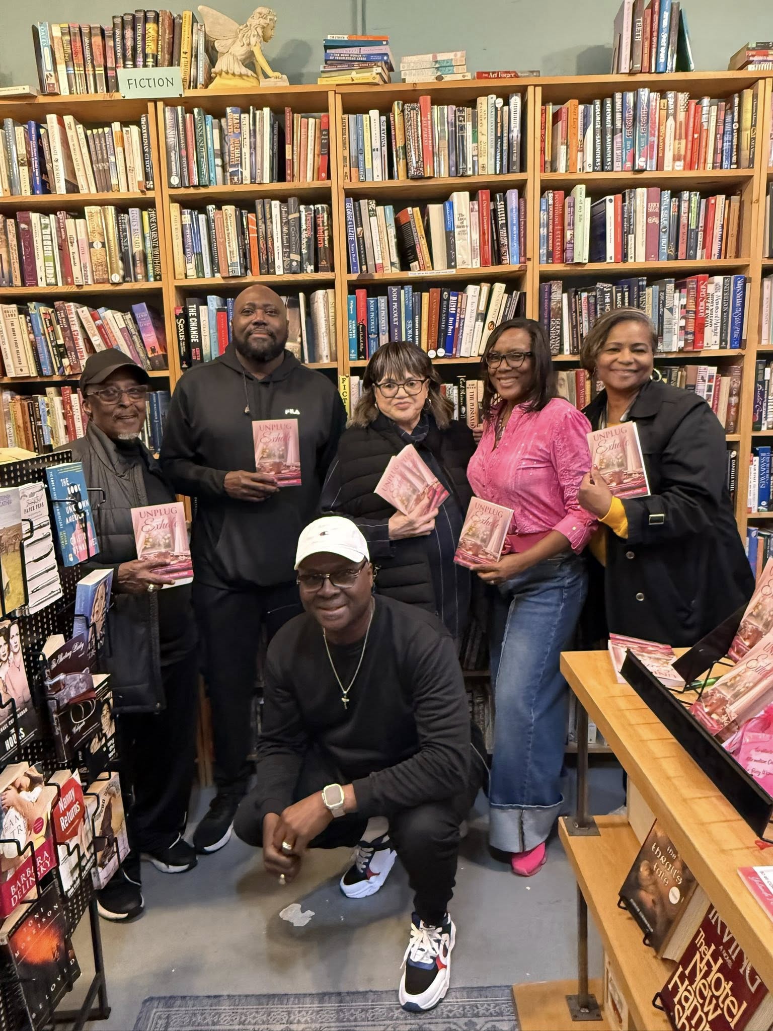 Six people in a bookstore, some holding books, standing in front of tall bookshelves filled with books.