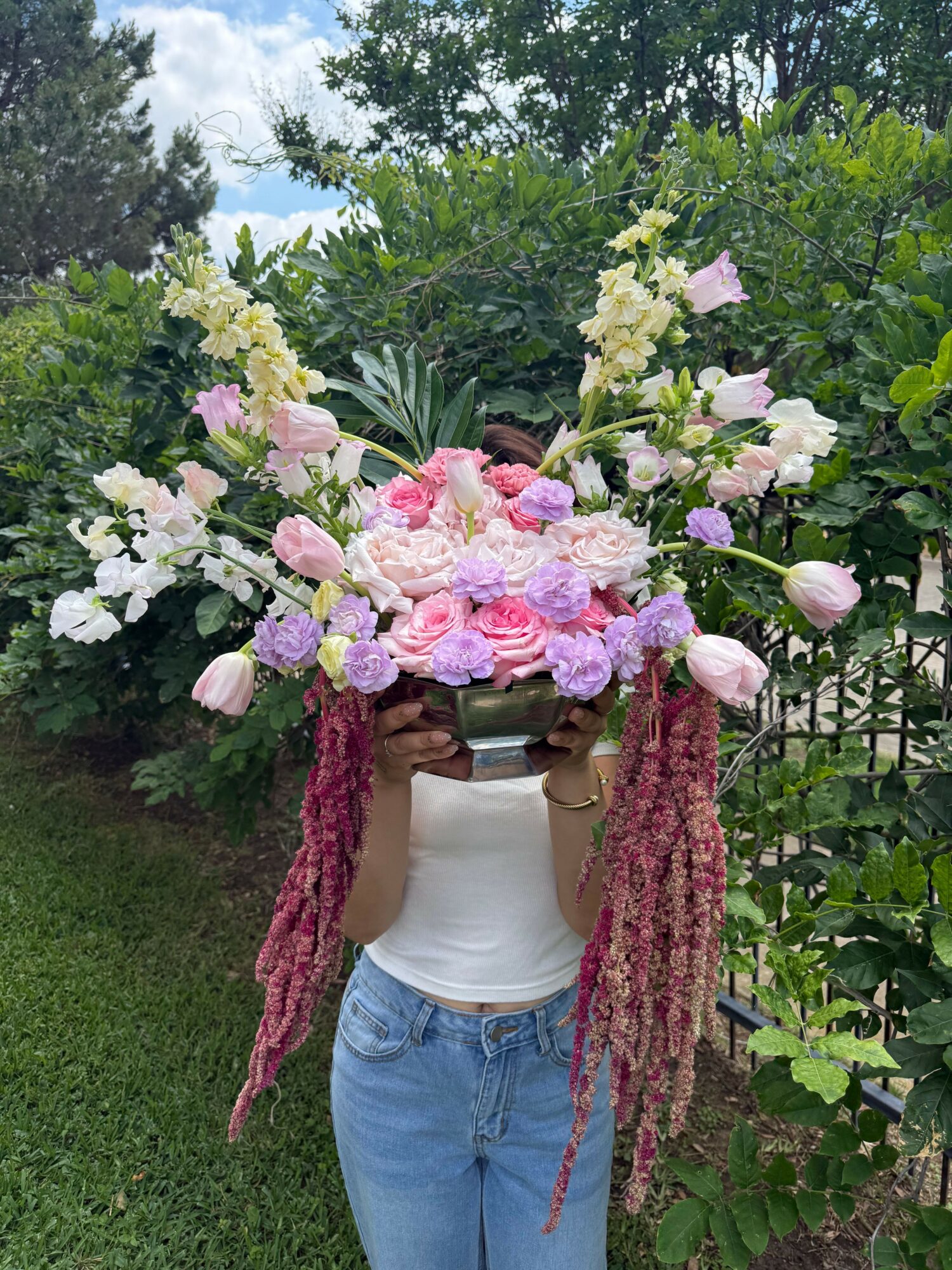 Person holding a large colorful flower bouquet outdoors, with trees and grass in the background.