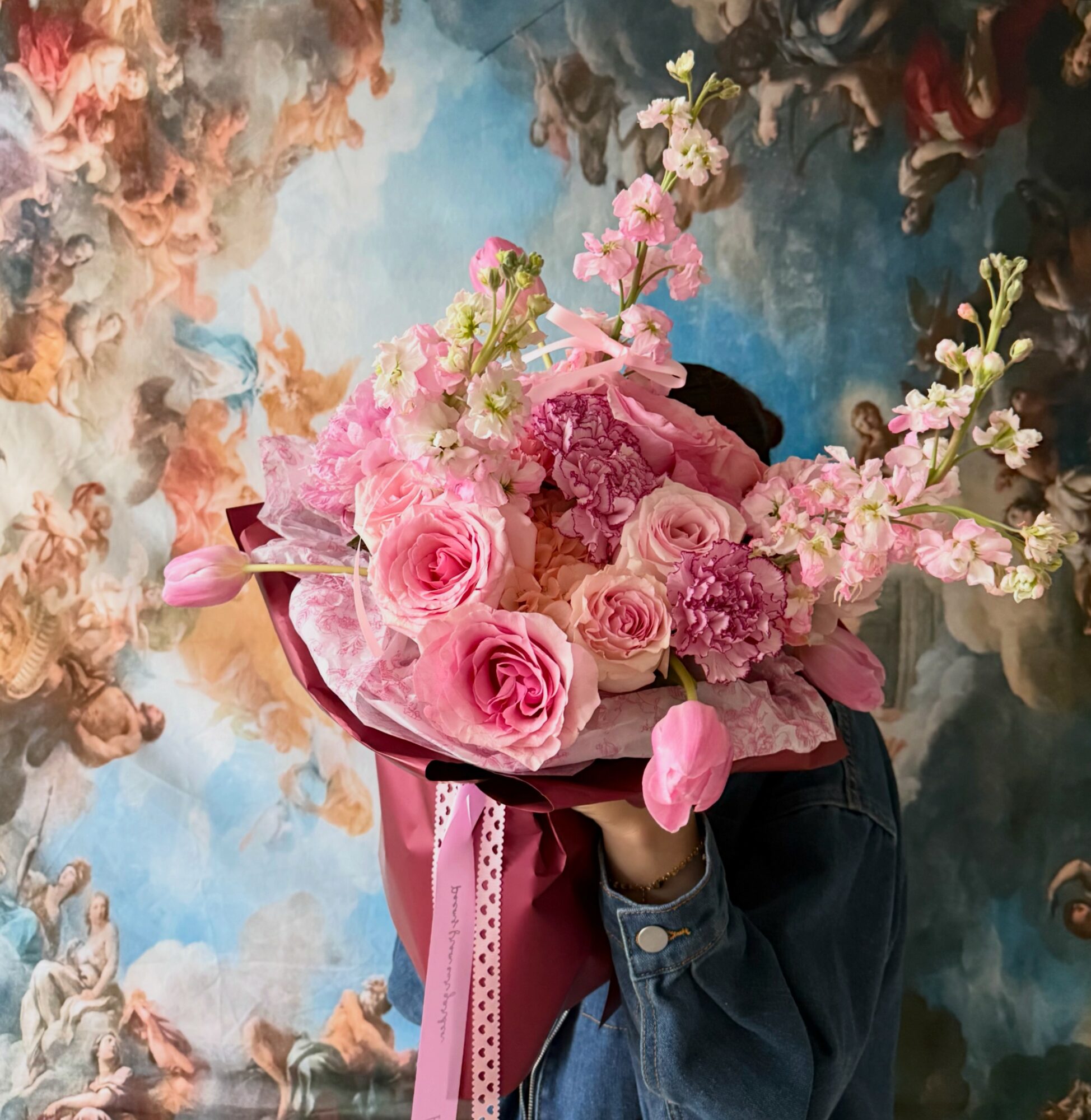 Person holding a large bouquet of pink roses and flowers, with a colorful abstract background.