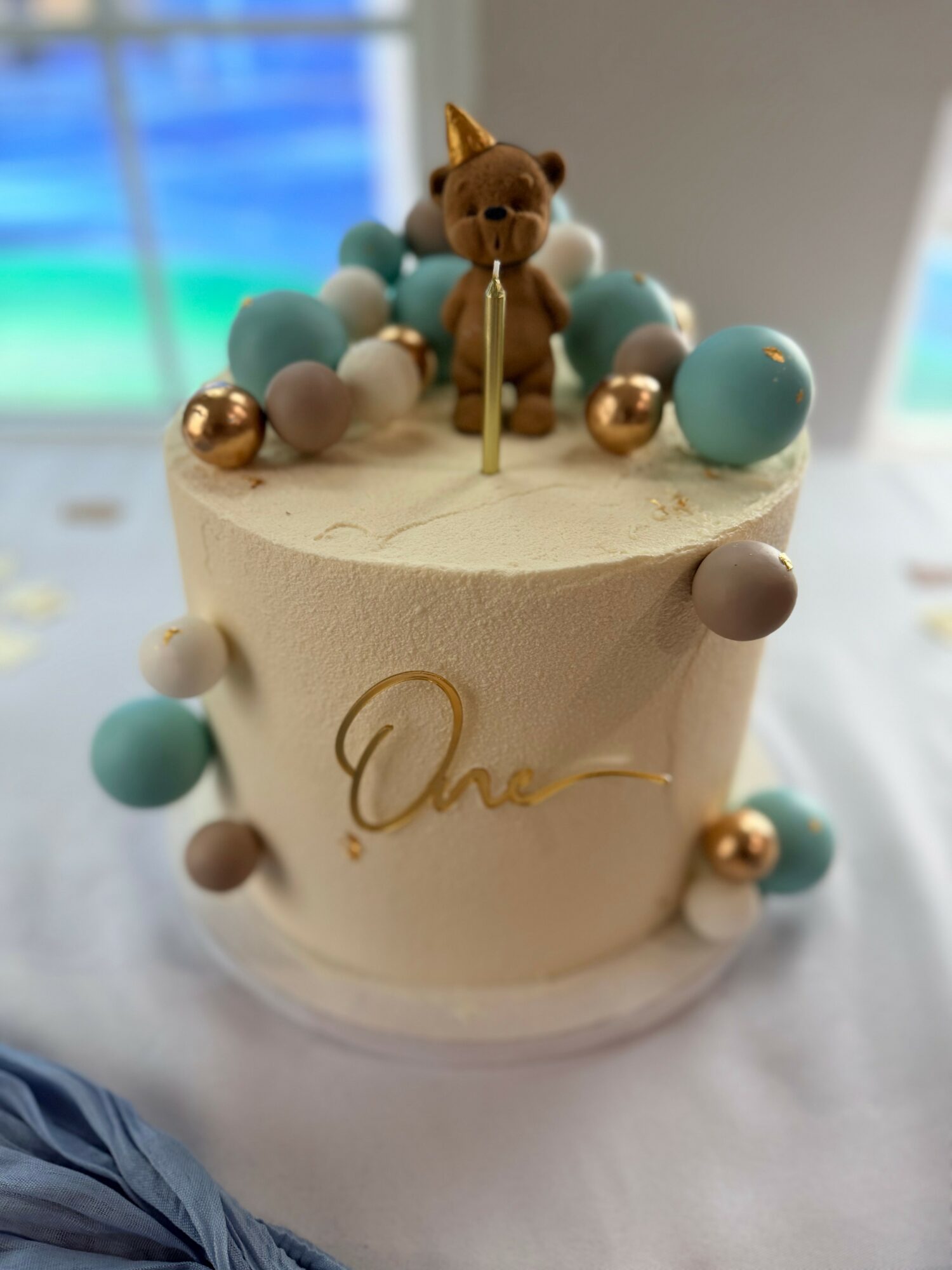 Cake with a cat figurine, decorated with pastel and metallic spheres, and a gold script on the side.