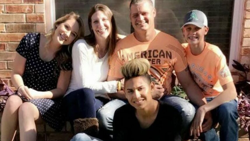 Group of five people sitting outdoors, smiling, with a brick wall background.