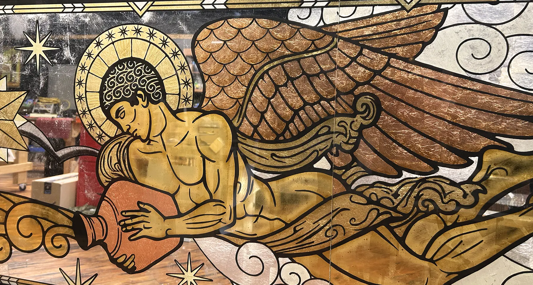 A stained glass depiction of a reclining angel with wings, a halo, and a contemplative expression, surrounded by clouds and stars.