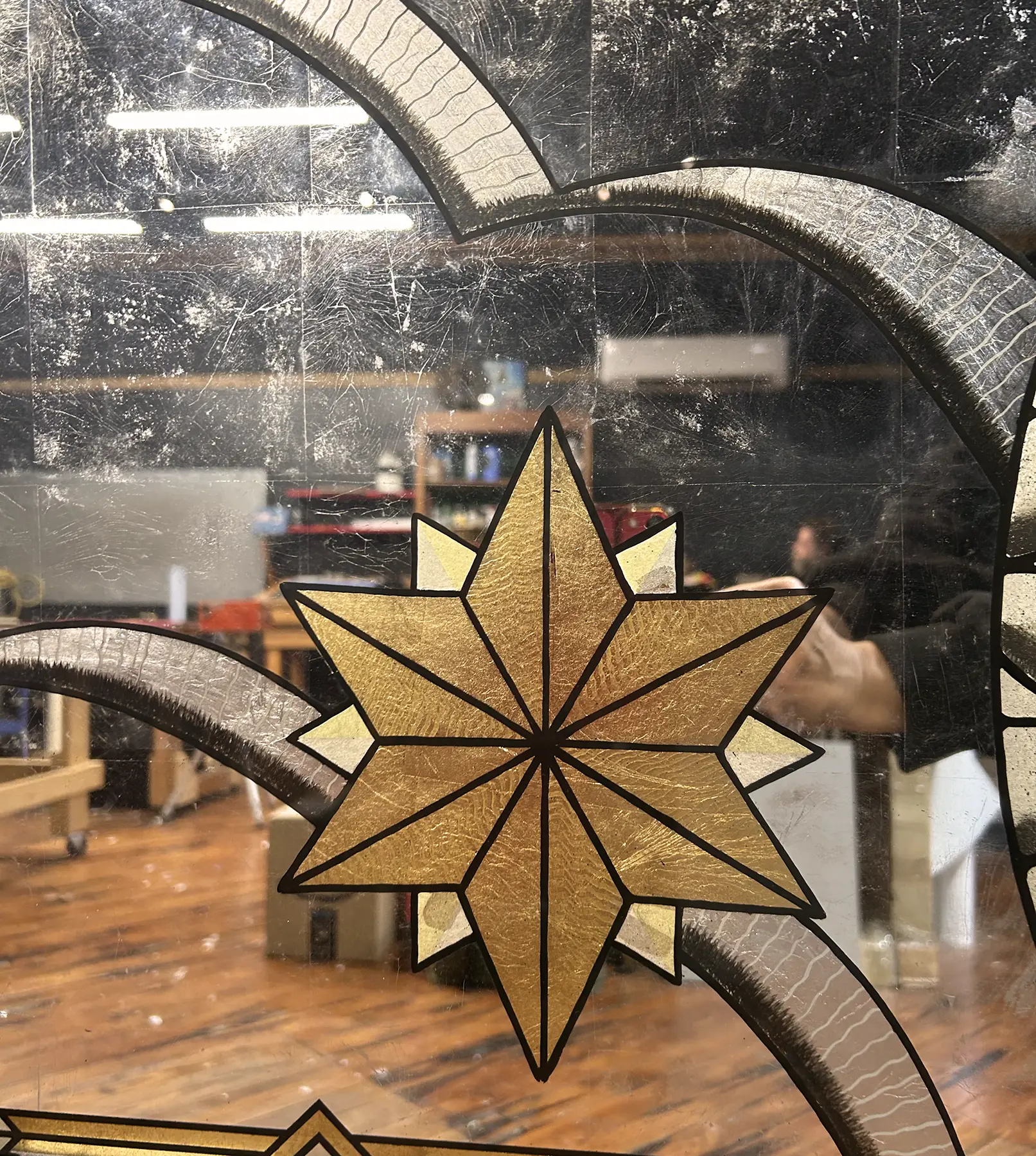 Decorative star-shaped stained glass with gold and red sections, reflected in a mirror, with a room and furniture in the background.