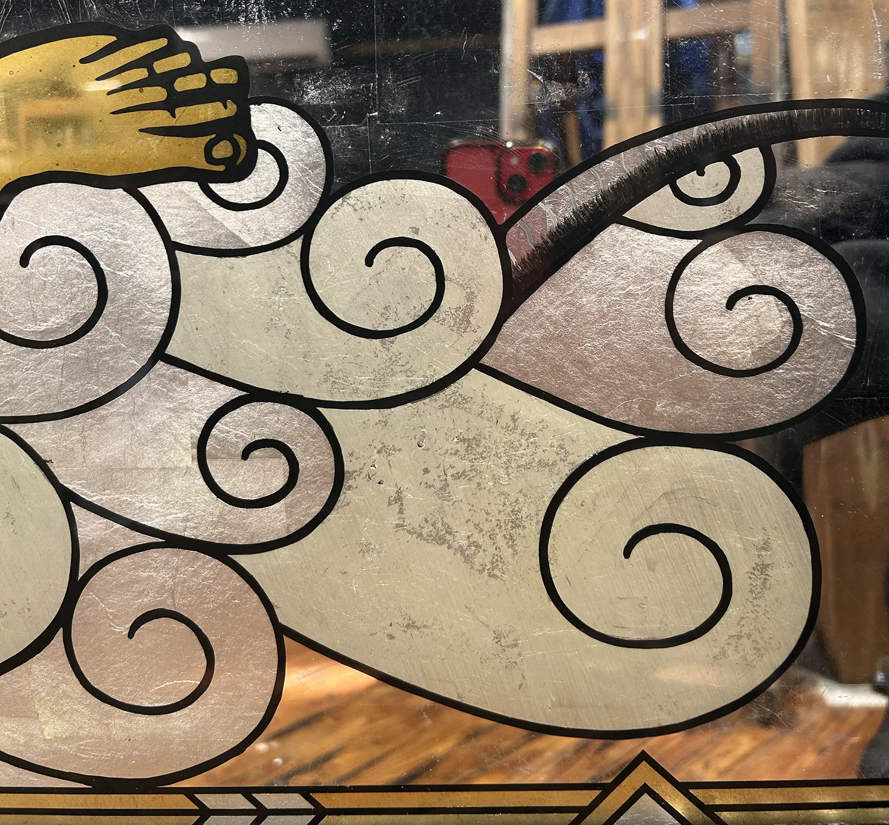 Decorative window with swirling cloud patterns and a hand at the top left, seen through glass with reflections.