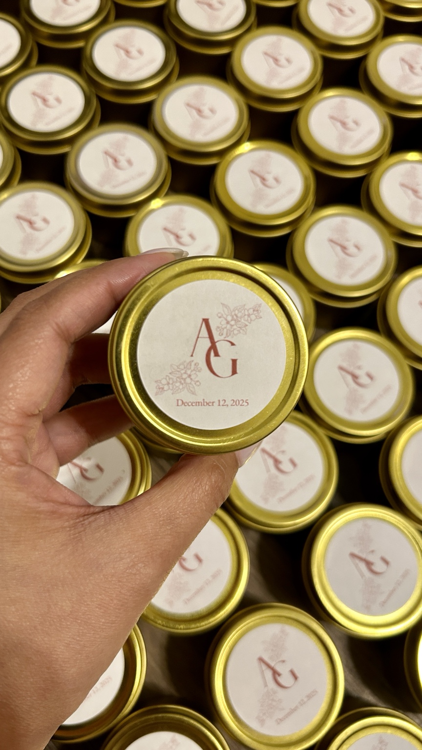 Hand holding a small round container with a gold rim, surrounded by similar containers, all with a white label and pink design.