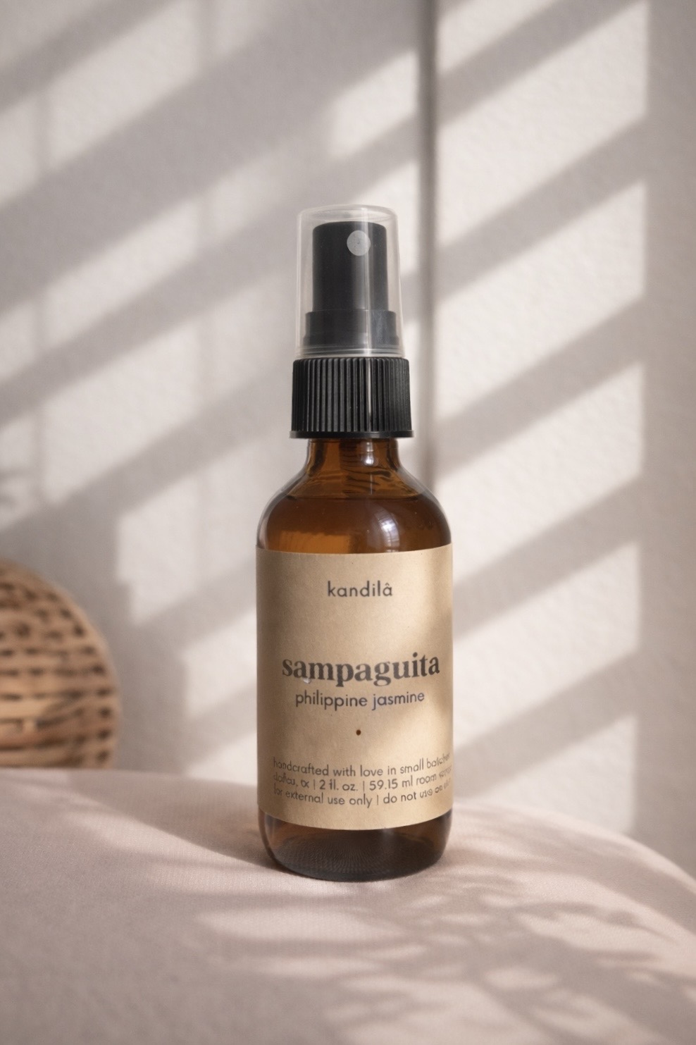 Small amber spray bottle with a black cap and label, placed on a surface with shadows from window blinds.