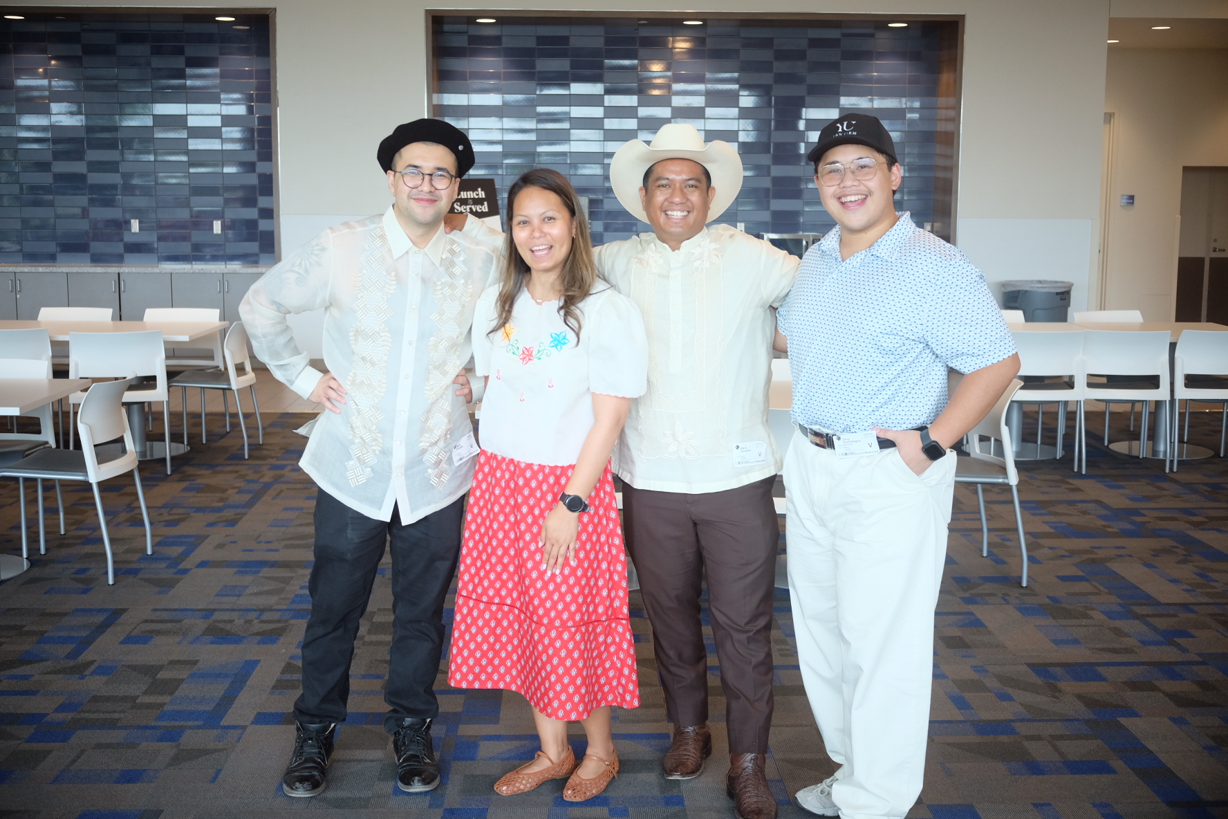 Four people standing together in a room with tables and chairs, smiling at the camera.