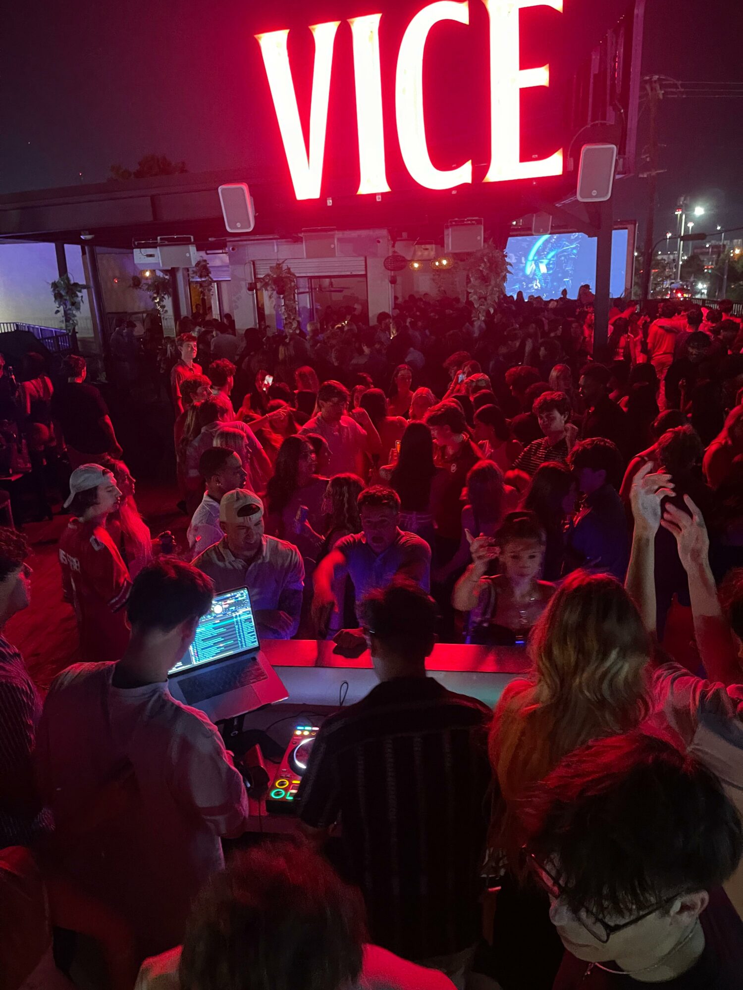 Crowd of people at a nighttime event with a large illuminated 'VICE' sign overhead.