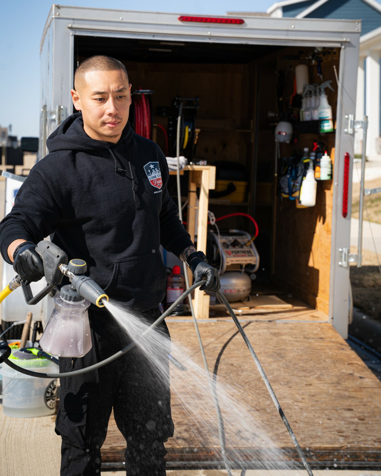 Person wearing a black hoodie cleaning the floor of a trailer with a spray nozzle.