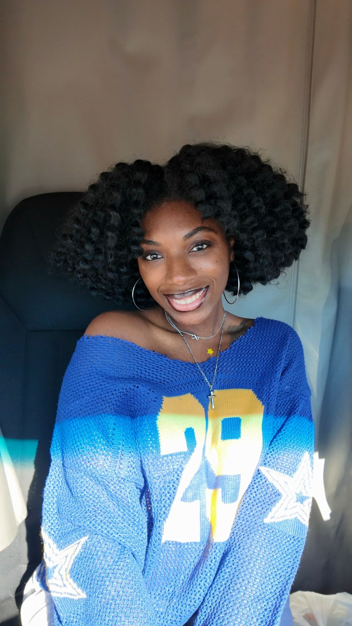 Smiling woman with curly hair wearing a blue sports jersey with yellow and white numbers and stars.