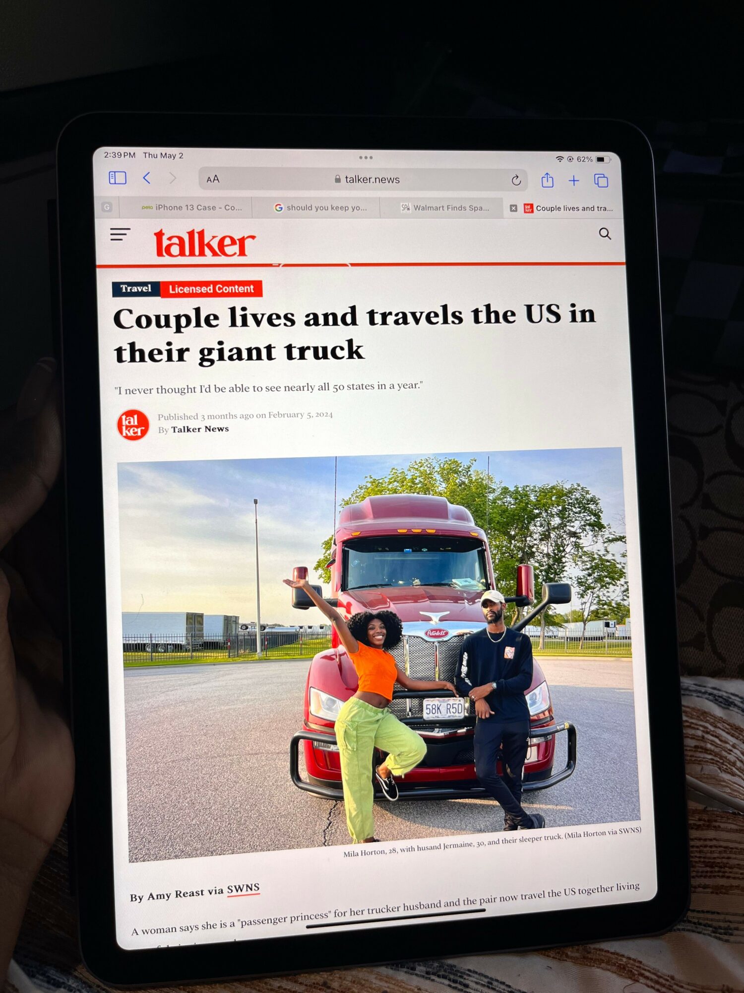 People loading items into a large truck on a road with trees and a blue sky.