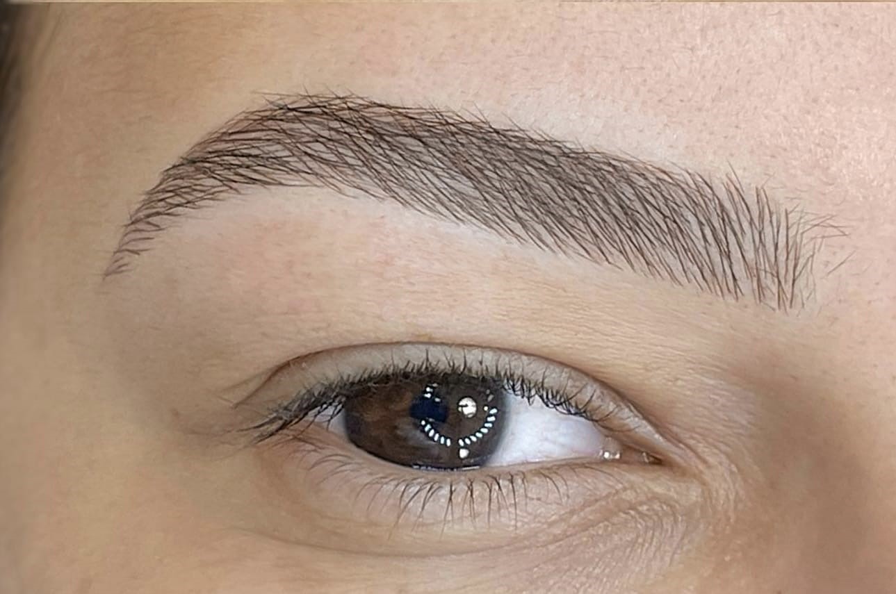 Close-up of a person's eye and eyebrow with natural skin tone and detailed eyebrow hairs.