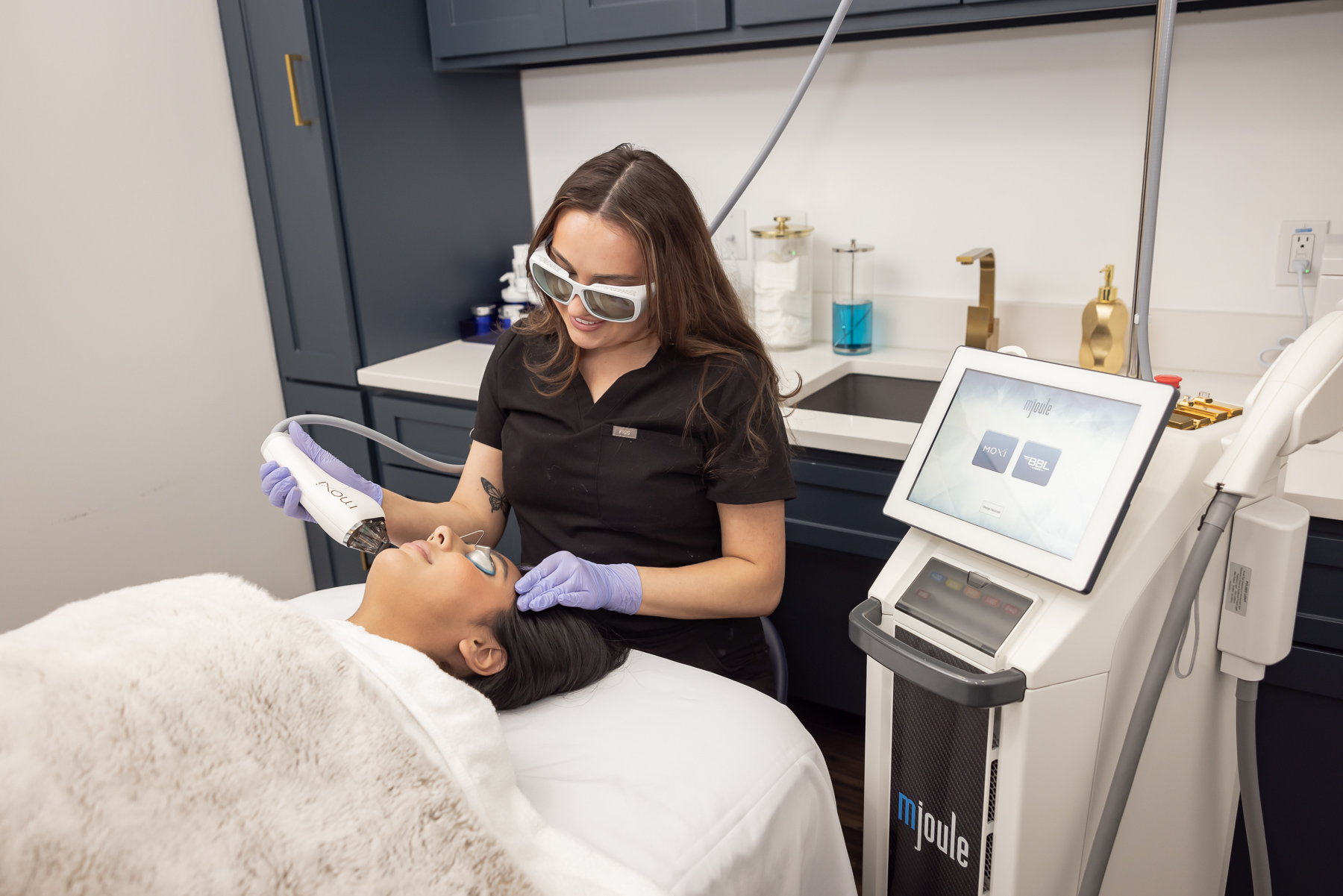 A woman in protective goggles and gloves performs a dental procedure on a patient lying in a dental chair in a clinic.