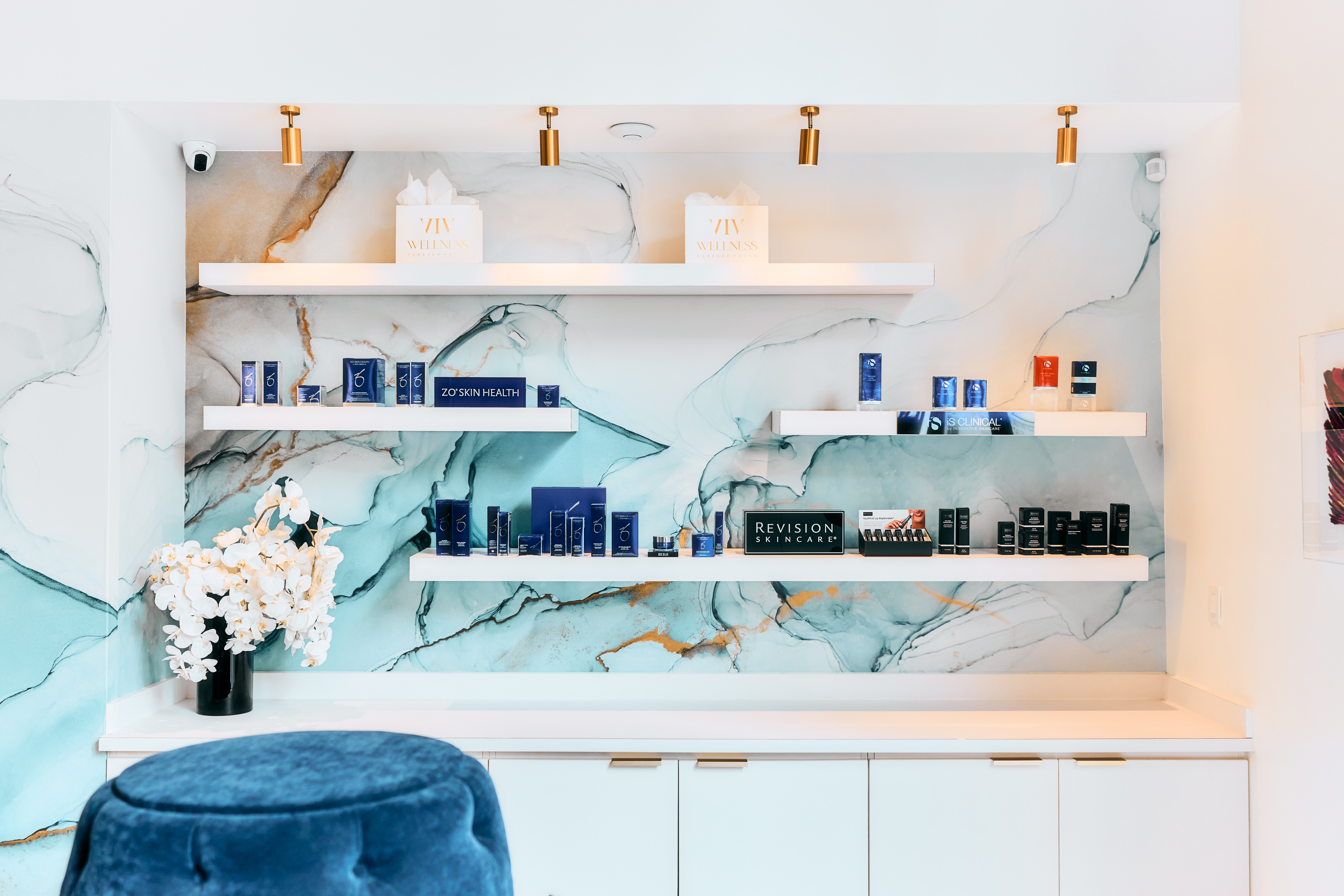 White marble wall with shelves holding blue and black electronic devices, a vase with white flowers, and decorative items.