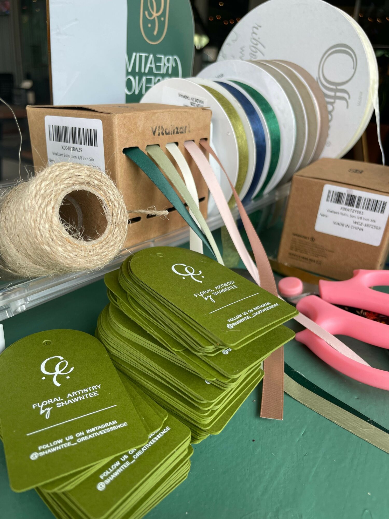 Stack of green cards, rolls of twine, and various paper plates and boxes on a table.