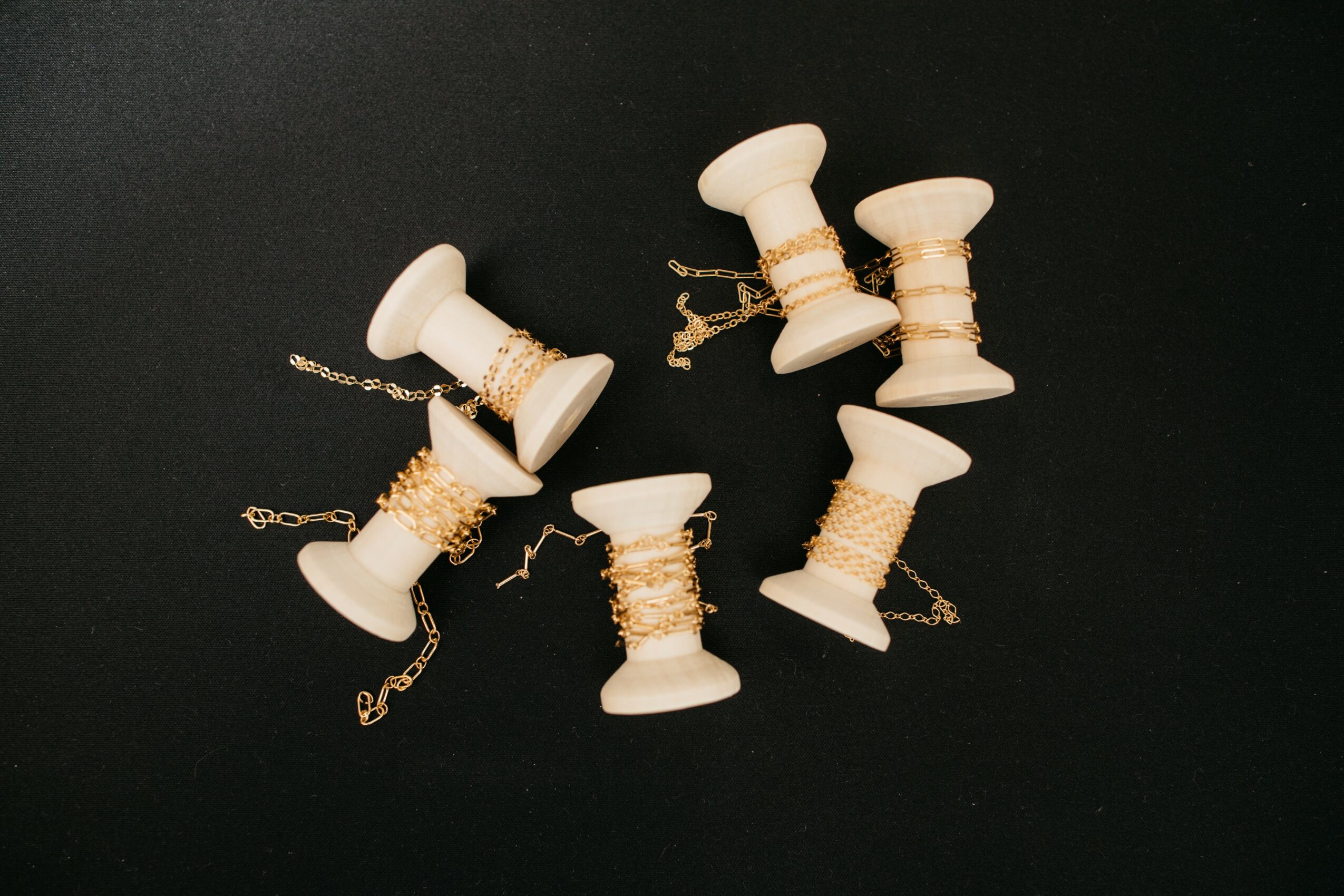 Six white spools with gold thread and chains scattered on a black background.