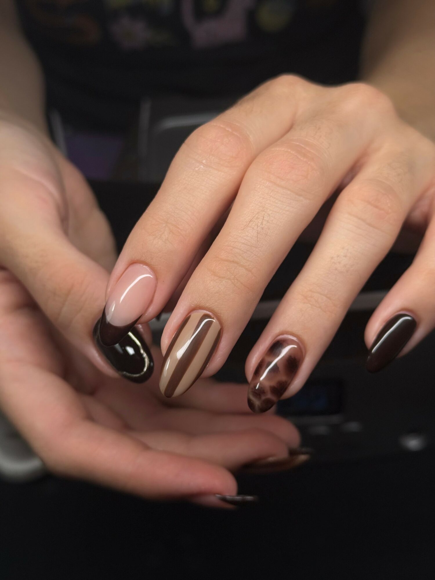Close-up of a hand with manicured nails featuring black, beige, and tortoiseshell designs.