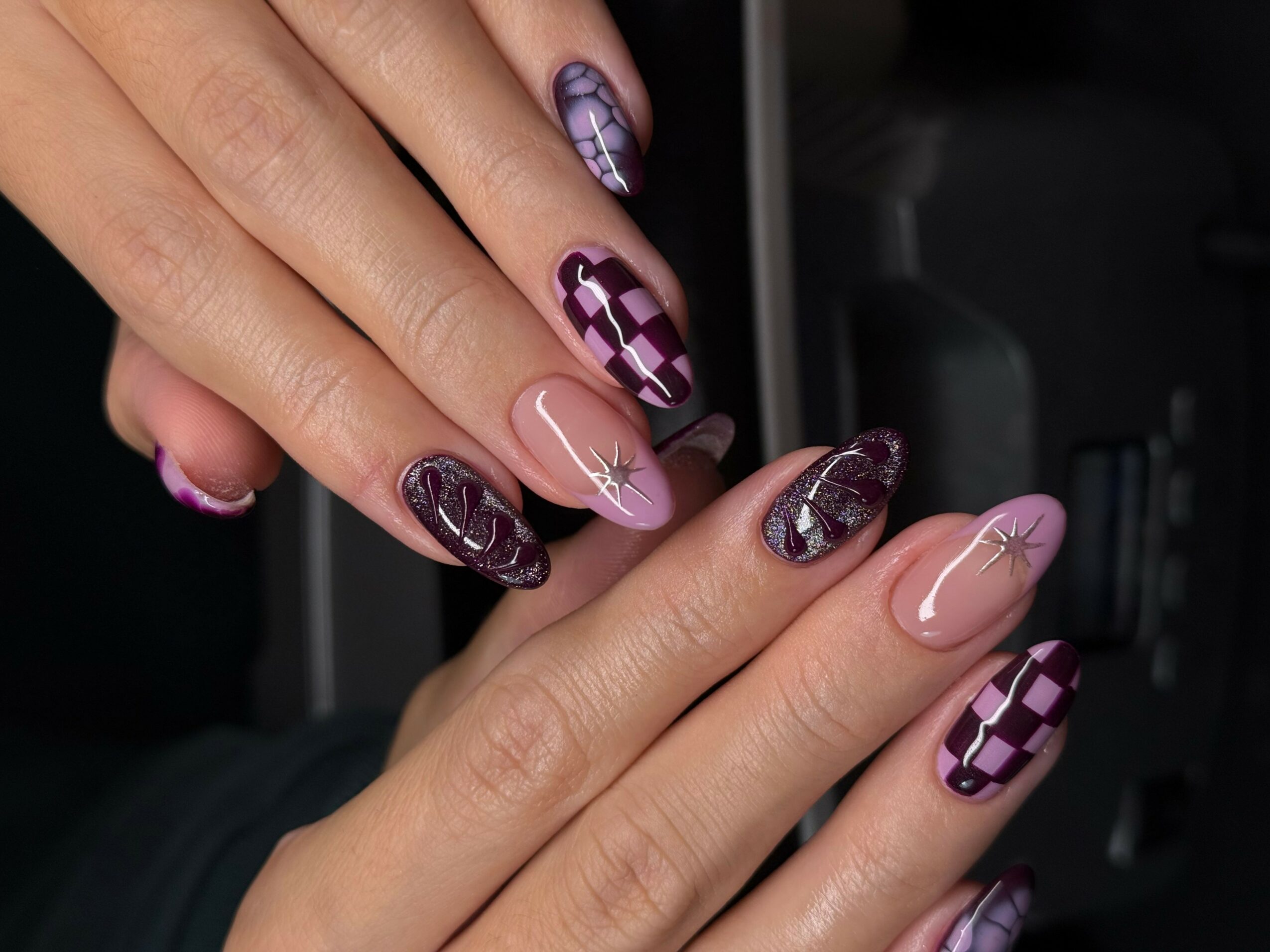 Close-up of hands with decorated nails, featuring purple, pink, and nude colors with geometric and star designs.