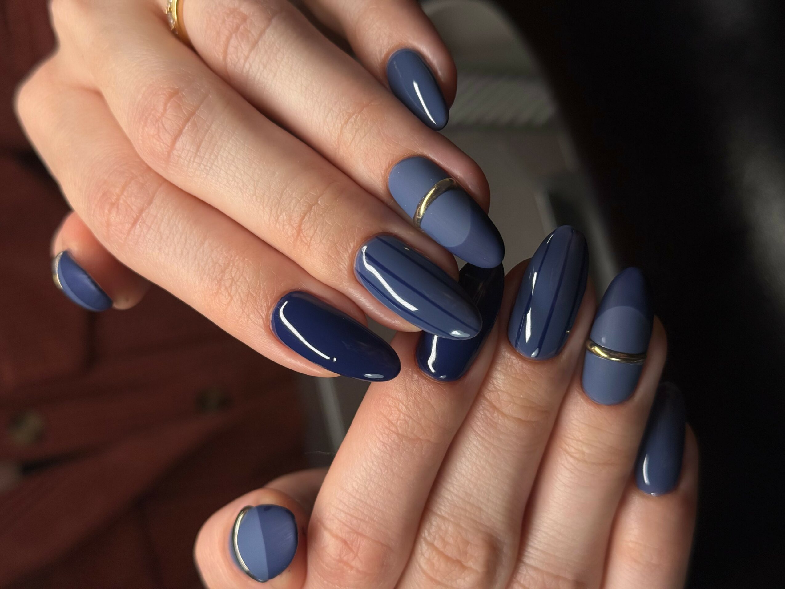 Close-up of hands with blue and gray nail polish, some nails have gold lines, nails are well-manicured.