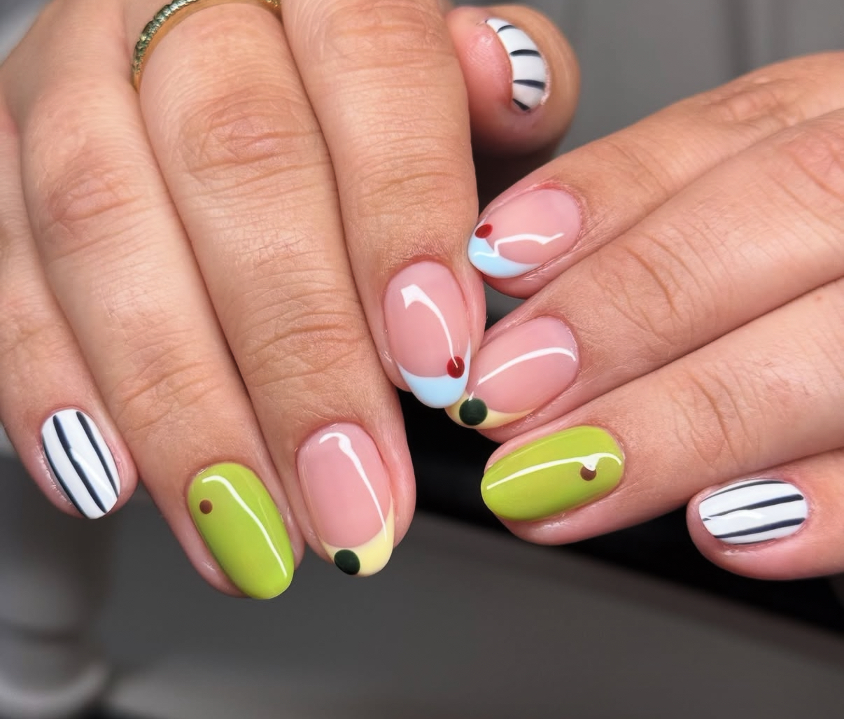 Hands with colorful, patterned nail art, including stripes, dots, and solid colors, on fingernails.