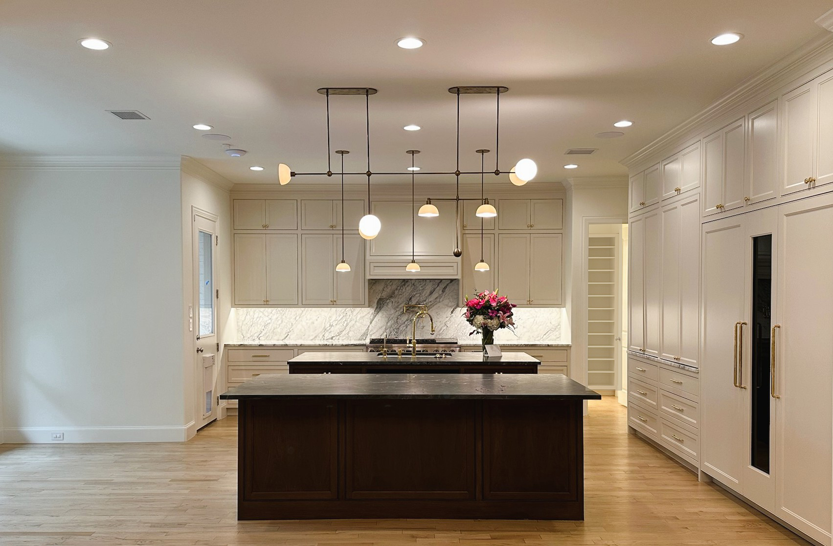 Modern kitchen with white cabinets, a central island with dark wood base, and pendant lights hanging above. Flowers on the island.
