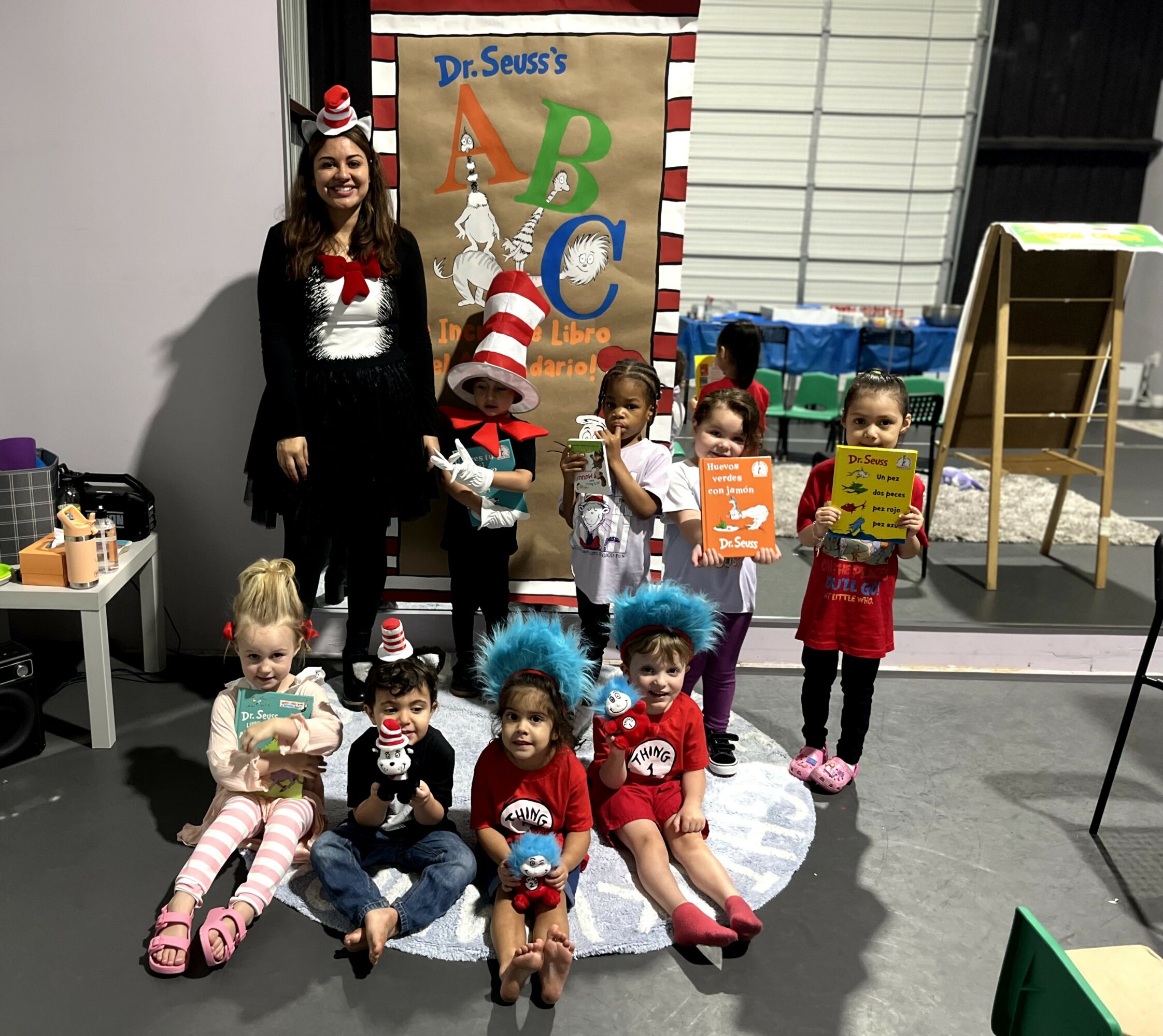 Group of children and a woman in festive costumes pose in front of a Dr. Seuss-themed display, some holding books.