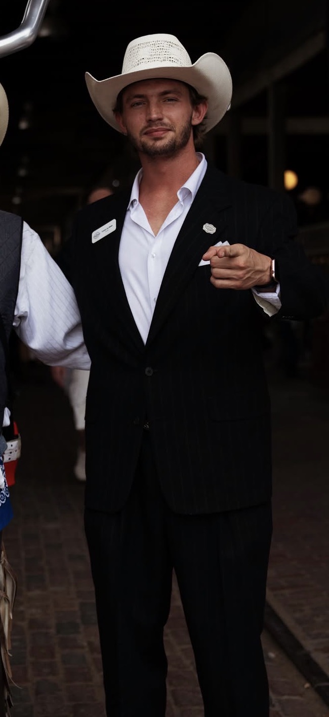 Man in a black suit, white shirt, and cowboy hat standing outdoors at night.