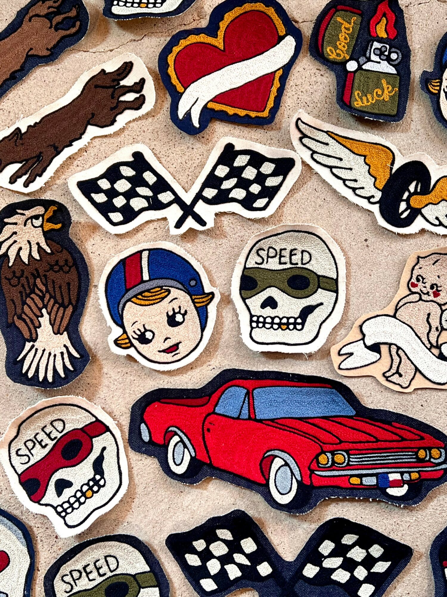 Collection of embroidered patches including a heart, skulls, a girl, a red car, an eagle, and checkered flags.