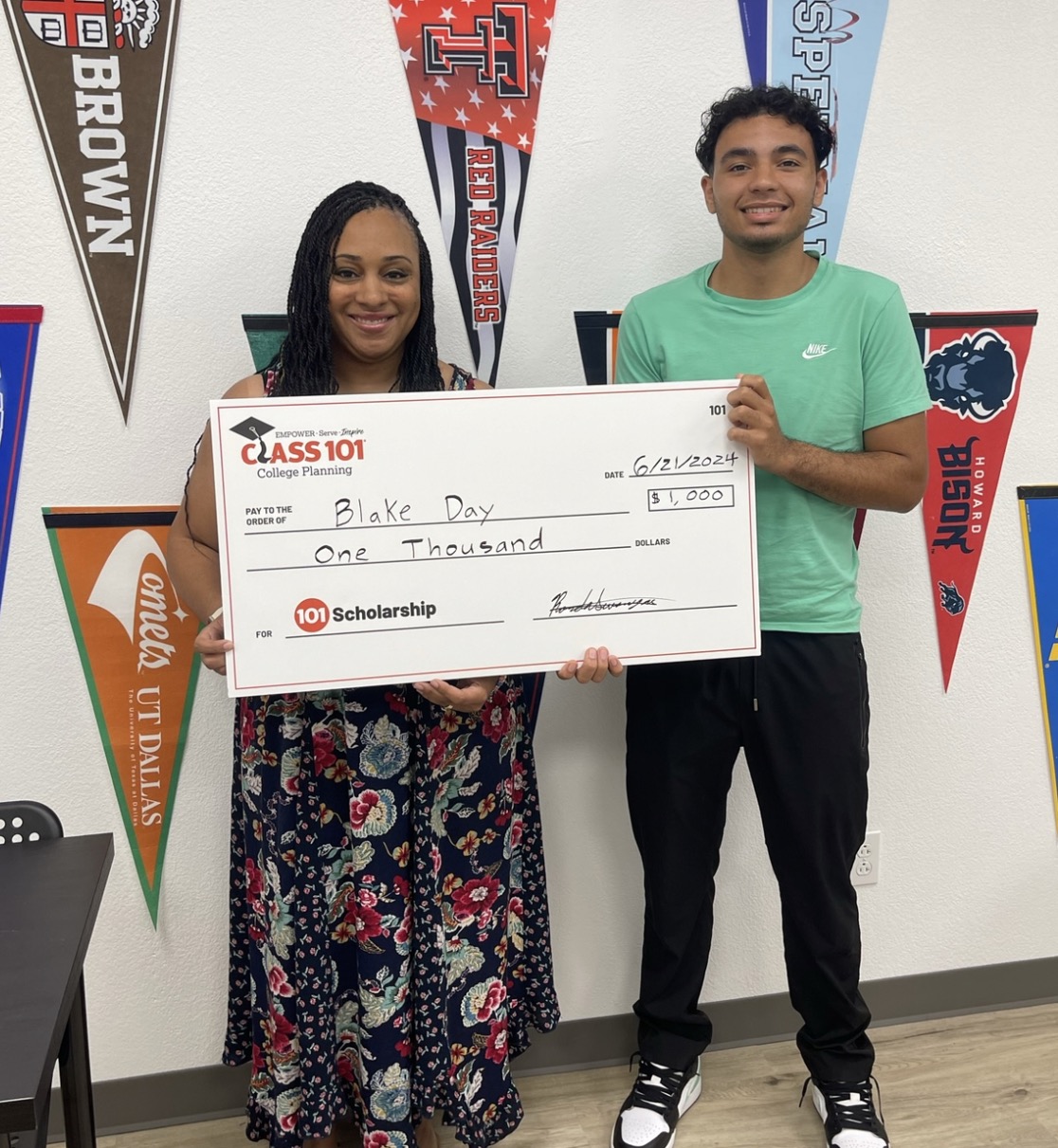 Two people holding a large check, standing in front of colorful pennant banners on a wall.