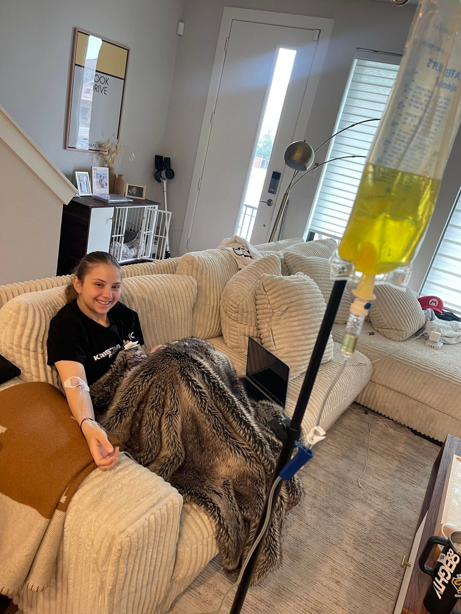 Person with long hair sitting on a beige sofa, cleaning with a yellow spray bottle, in a bright room with a door and window.