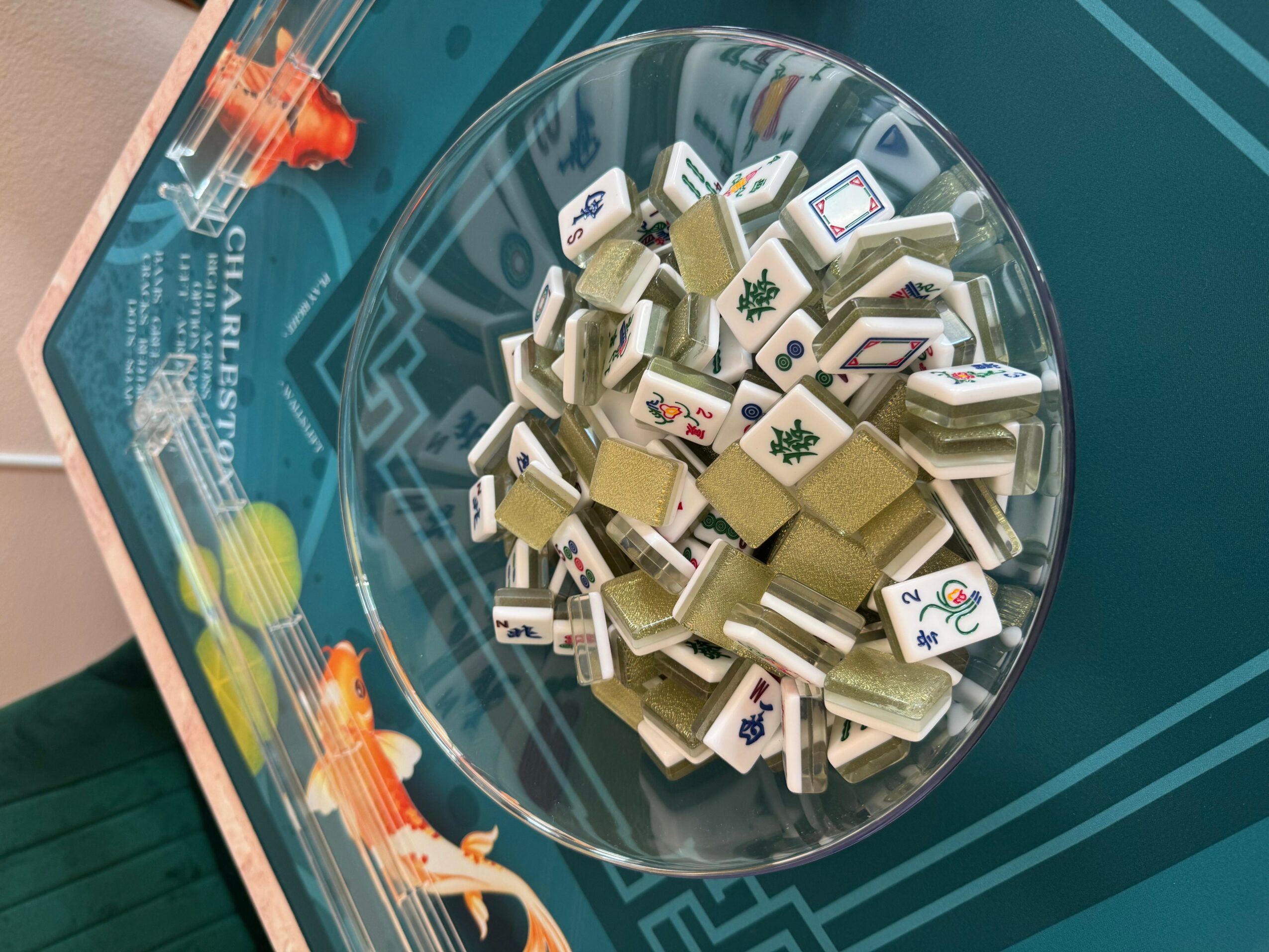 A bowl filled with Mahjong tiles on a table with a game board underneath.