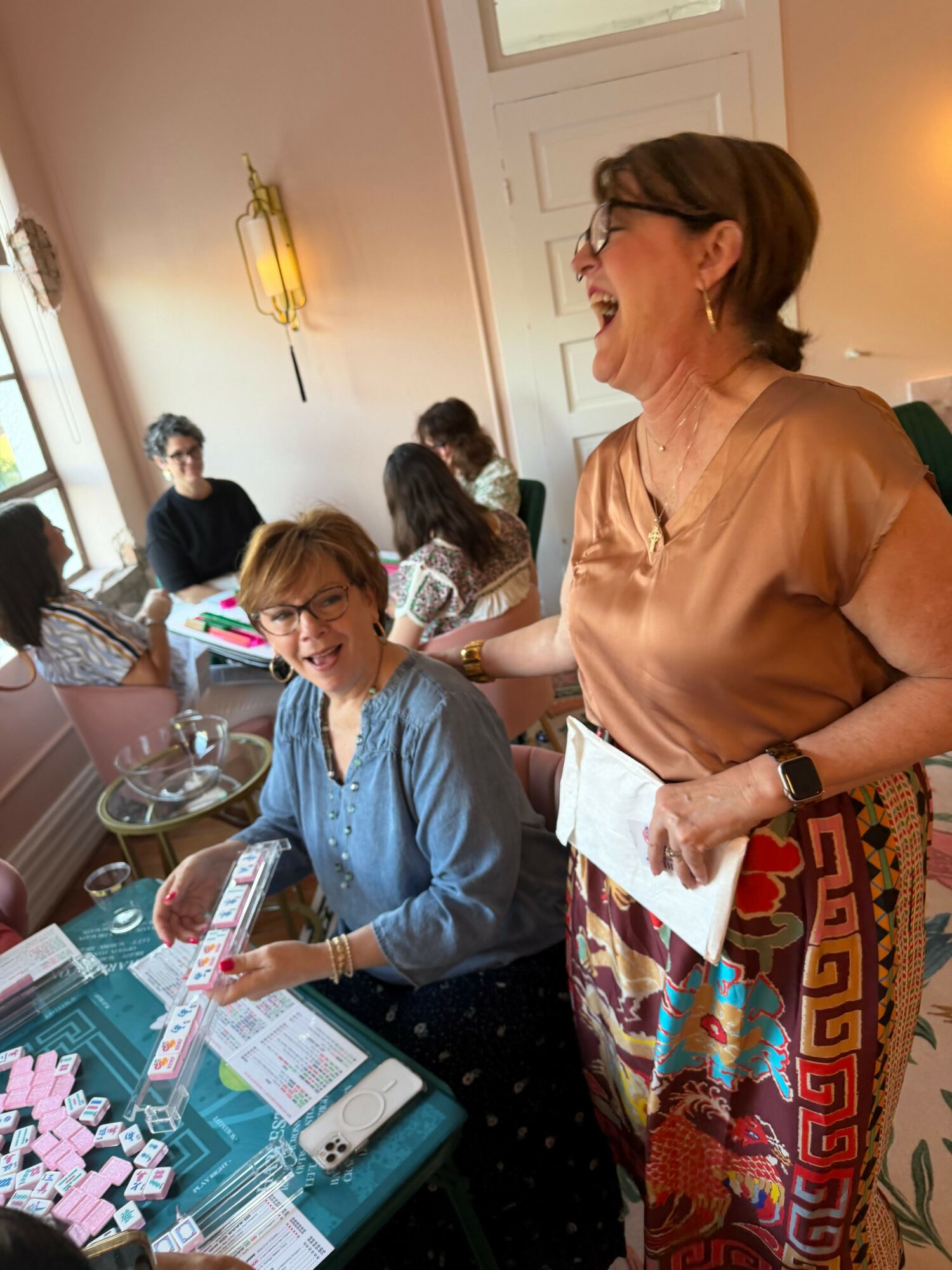 People gathered around a table with papers and sticky notes, woman standing and others sitting, in a room with a colorful blanket.