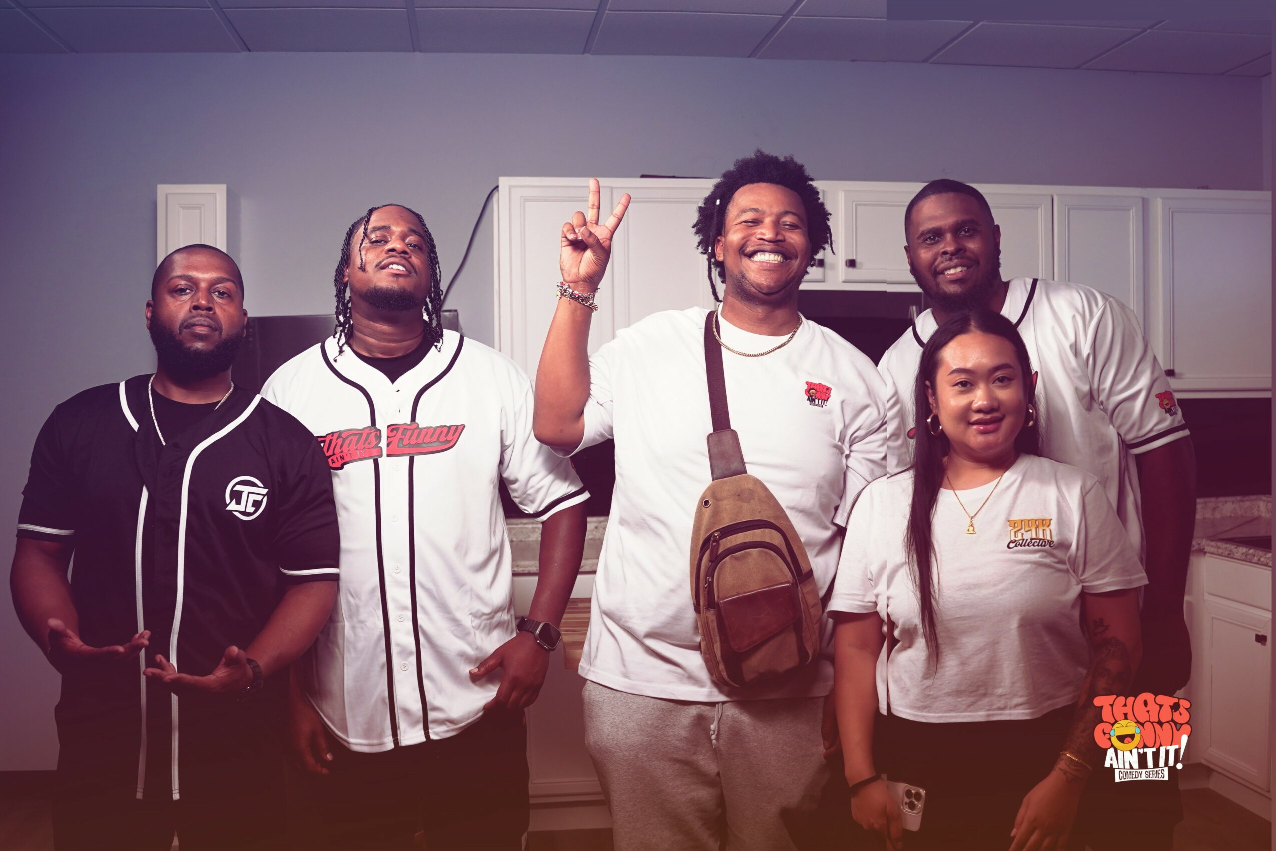 Group of five people standing indoors, smiling, with kitchen cabinets in the background.