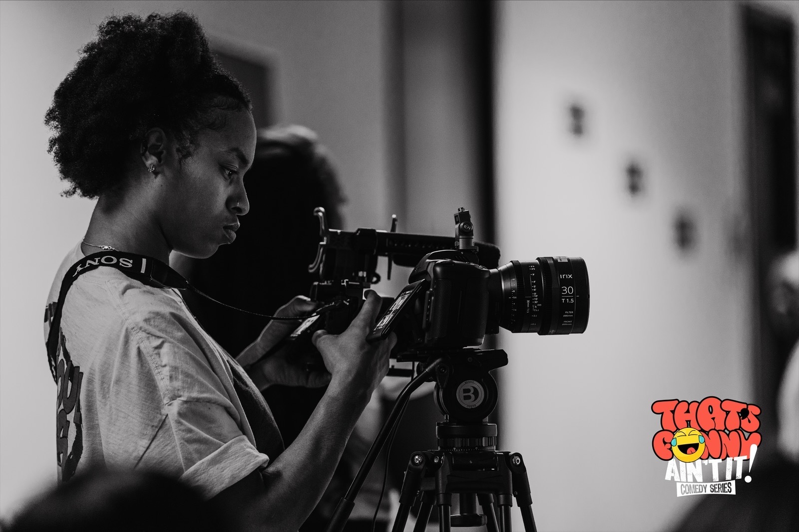 Young woman operating a professional camera on a tripod, focusing on filming, in black and white.
