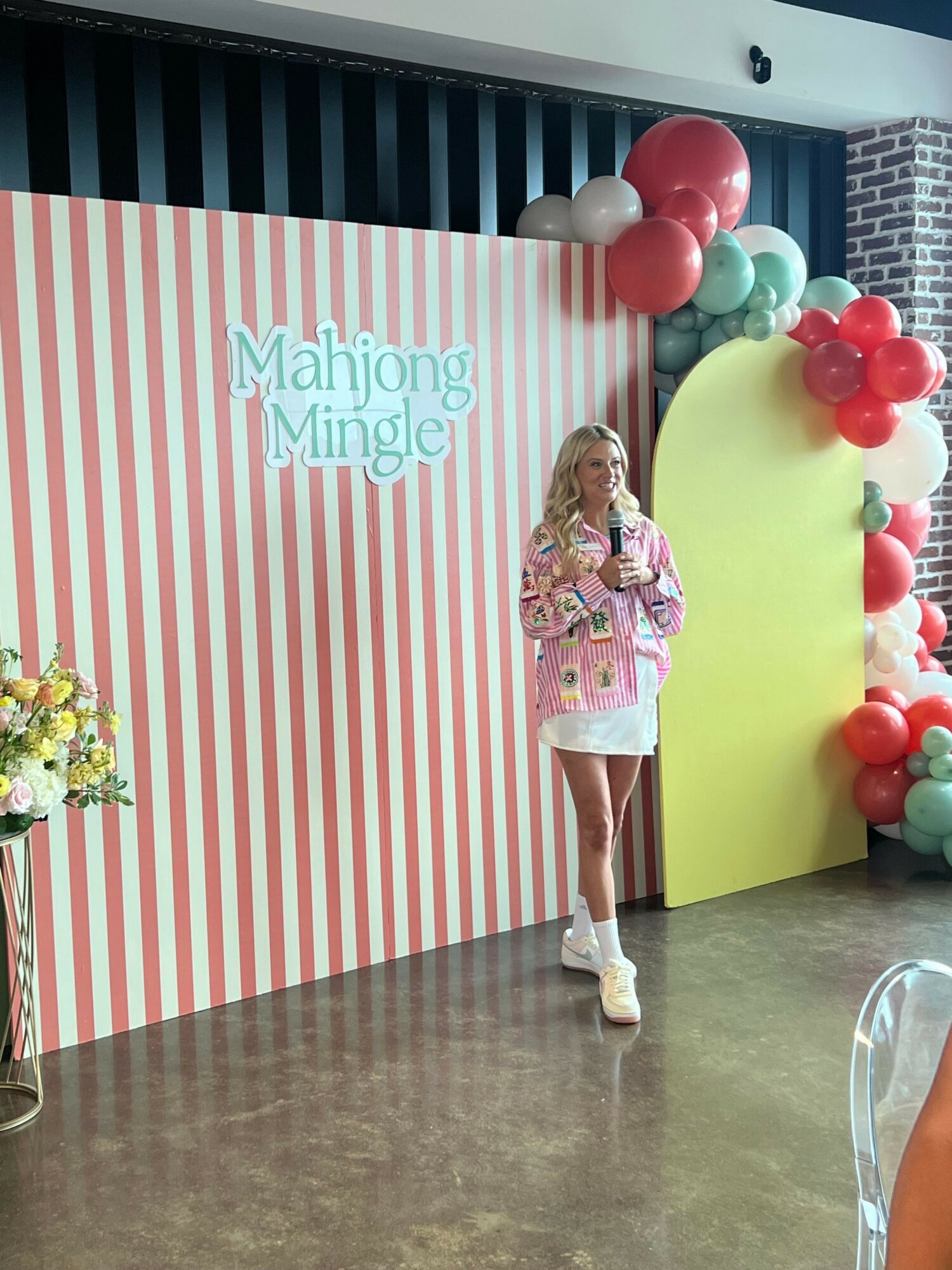 Child standing in front of a decorated backdrop with balloons and a striped background, holding a gift bag.