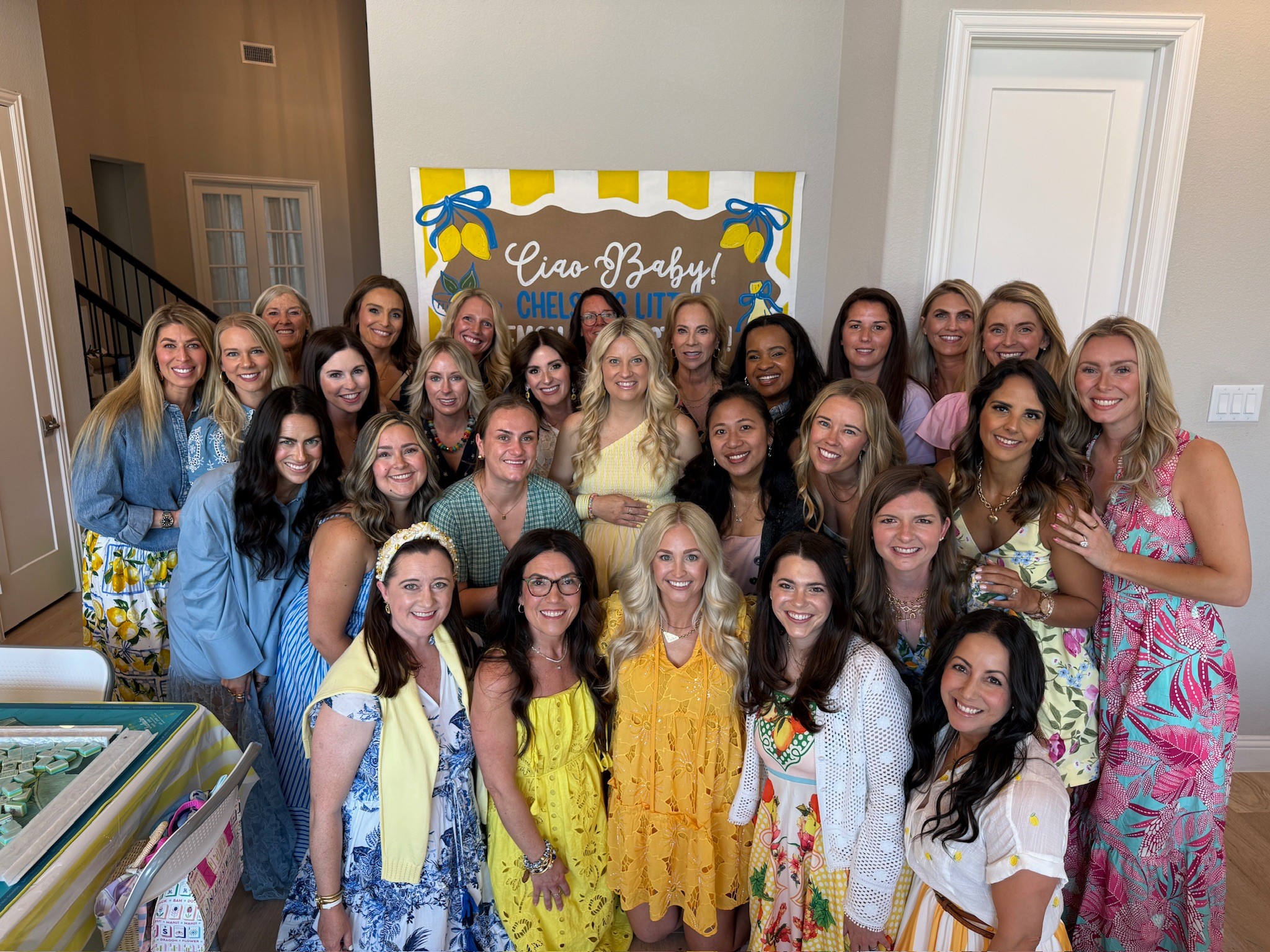 Group of women and girls gathered indoors in front of a colorful backdrop with text, smiling for a photo.