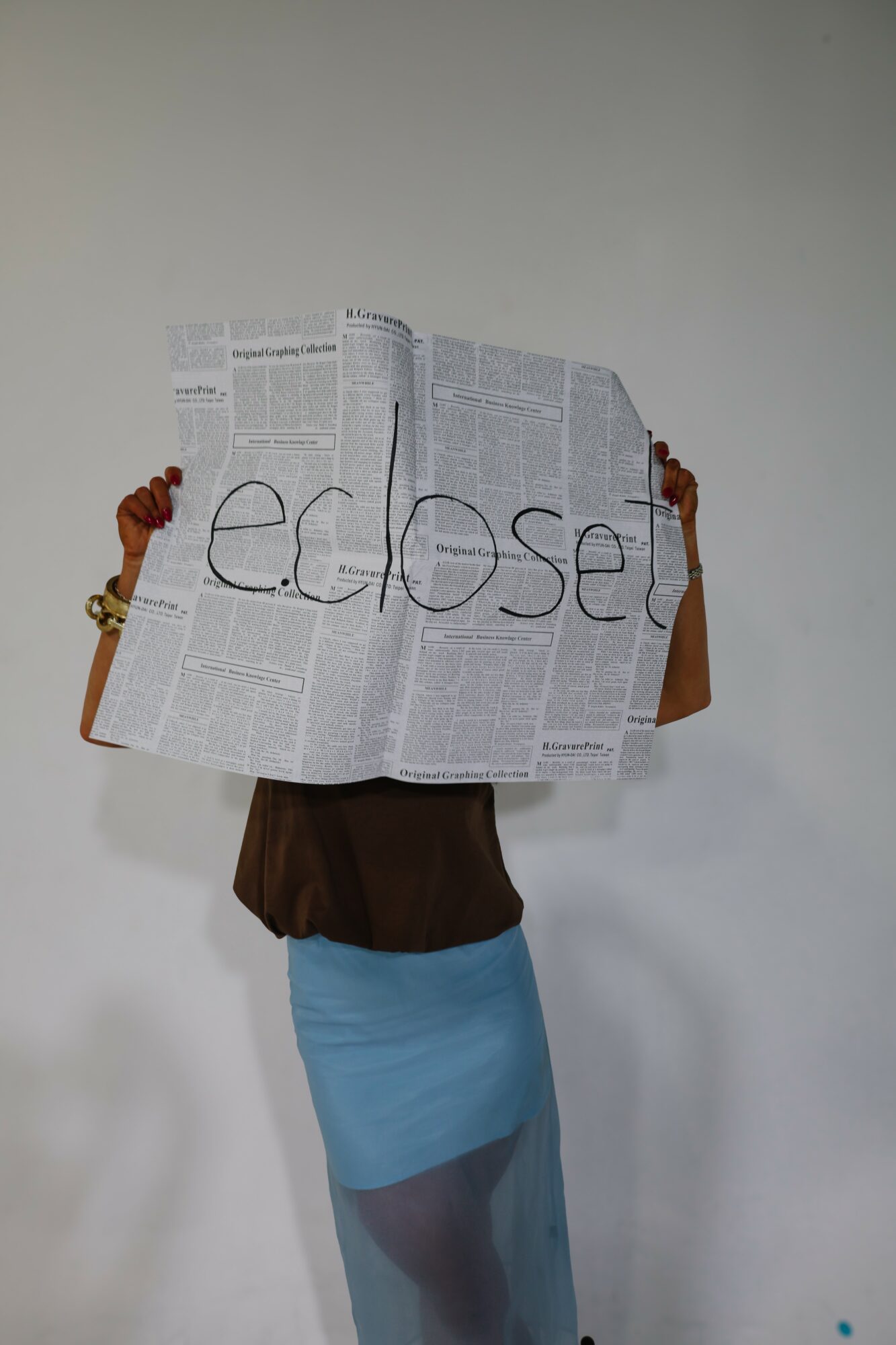 Person holding a newspaper with the word 'edbset' written on it, against a plain wall.