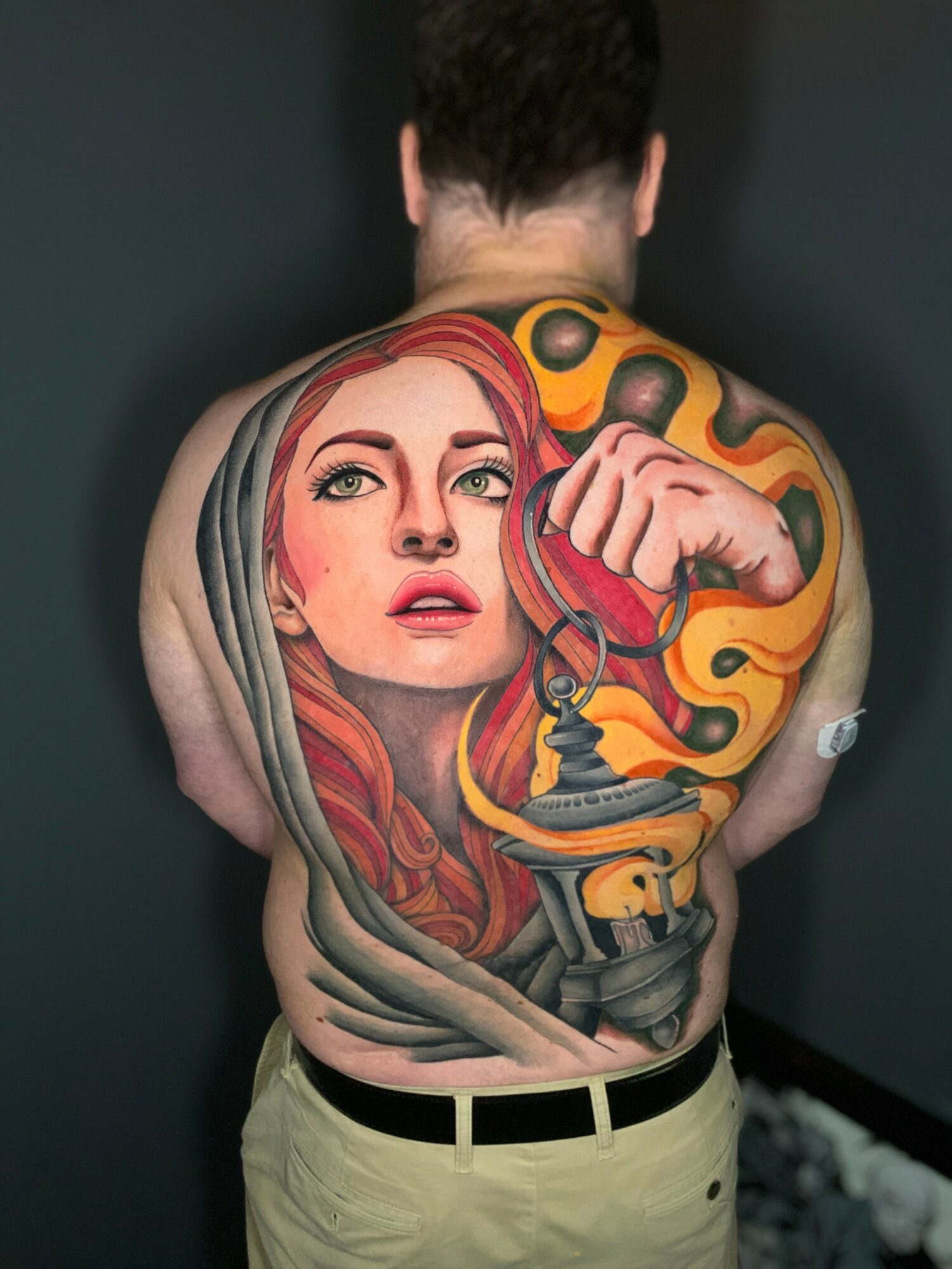 Back tattoo of a woman's face with red hair, surrounded by colorful abstract shapes and a gramophone, on a person's back.