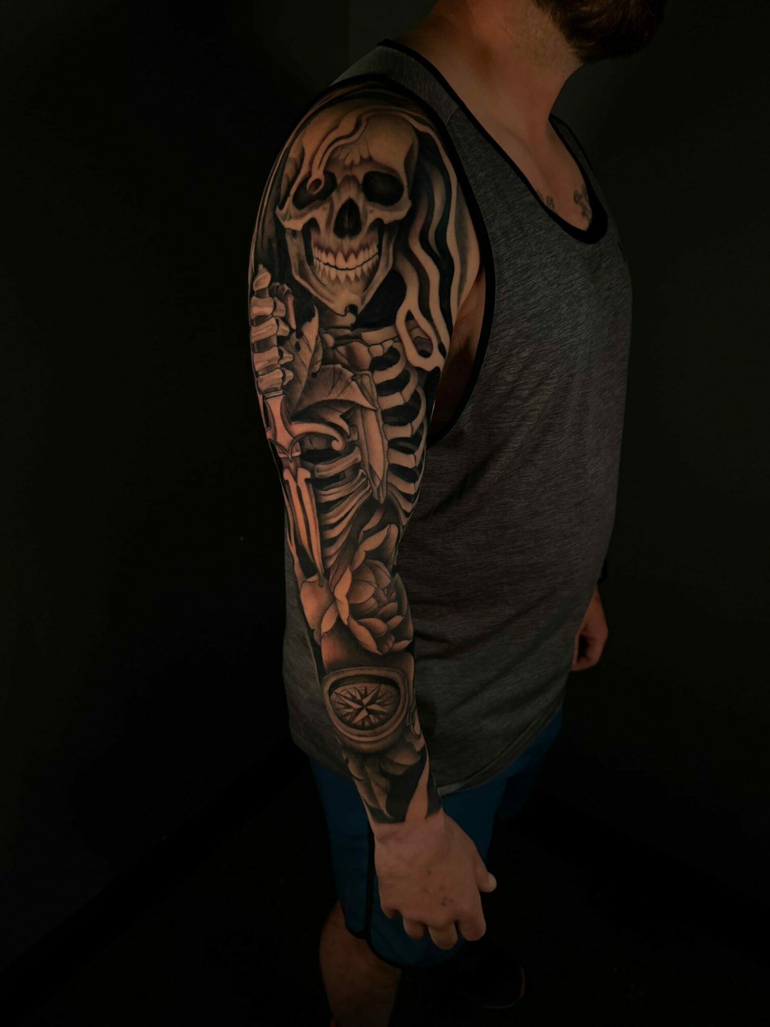 Person lying on side with a detailed skull and skeleton tattoo on arm, wearing a gray shirt and blue shorts.
